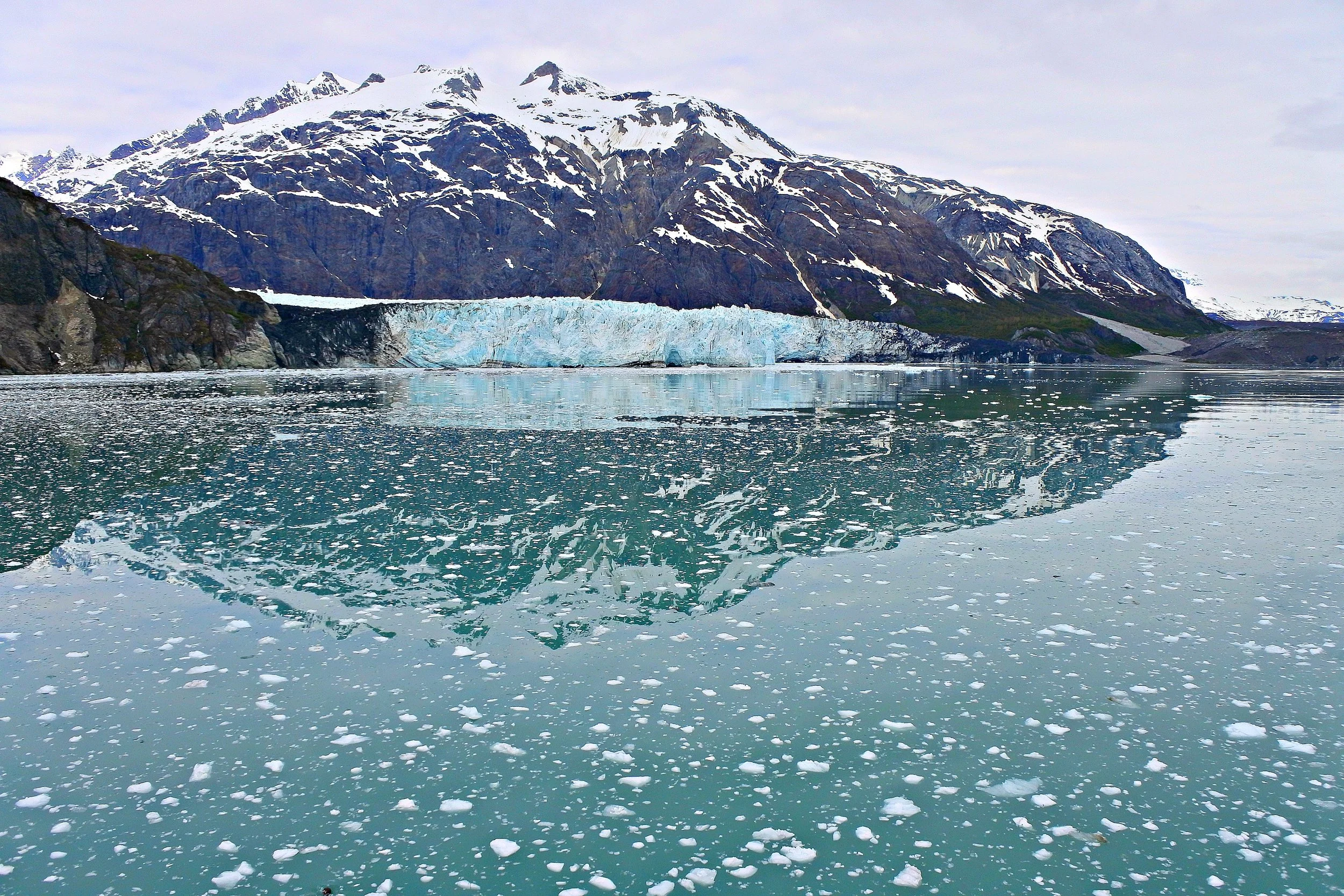 Glacier Bay, Alaska. The block of blue ice beneath the mountain is a glacier. The white fluff on the water are pieces of ice that broke away from the bigger block during a process called “caving”