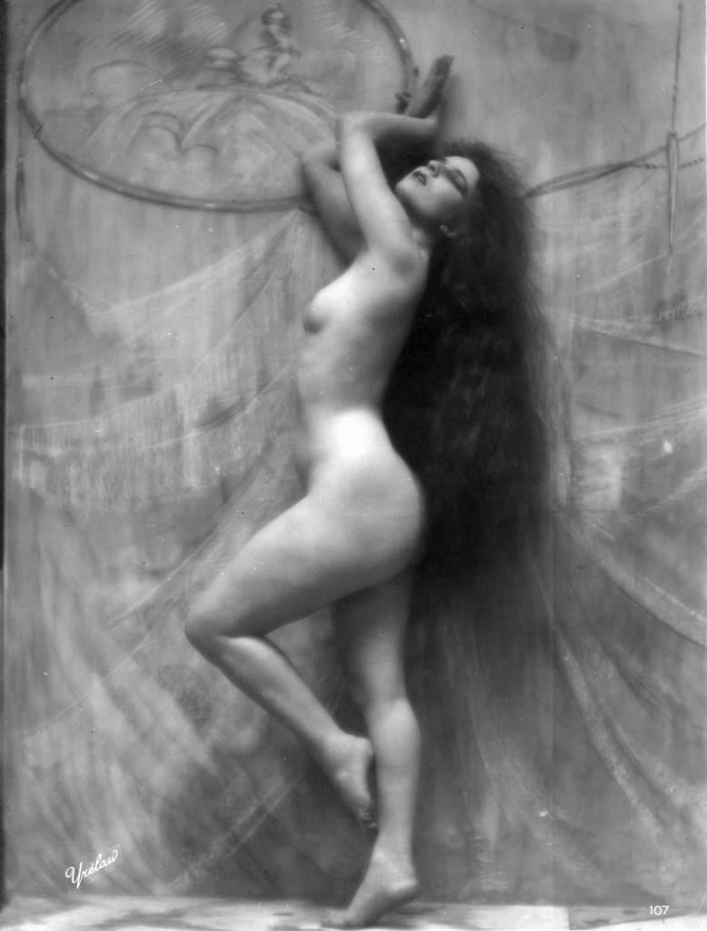 A nude woman with long dark hair strikes a graceful pose, circa 1900. 