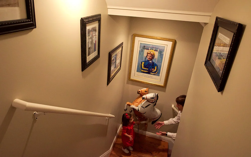 A portrait of legendary jockey Bill Shoemaker hangs in the stairwell of Hernandez's home in Louisville, as Hernandez and daughter Joshlyn play with horse balloons. Reminders of Hernandez's work are never far away, it seems.