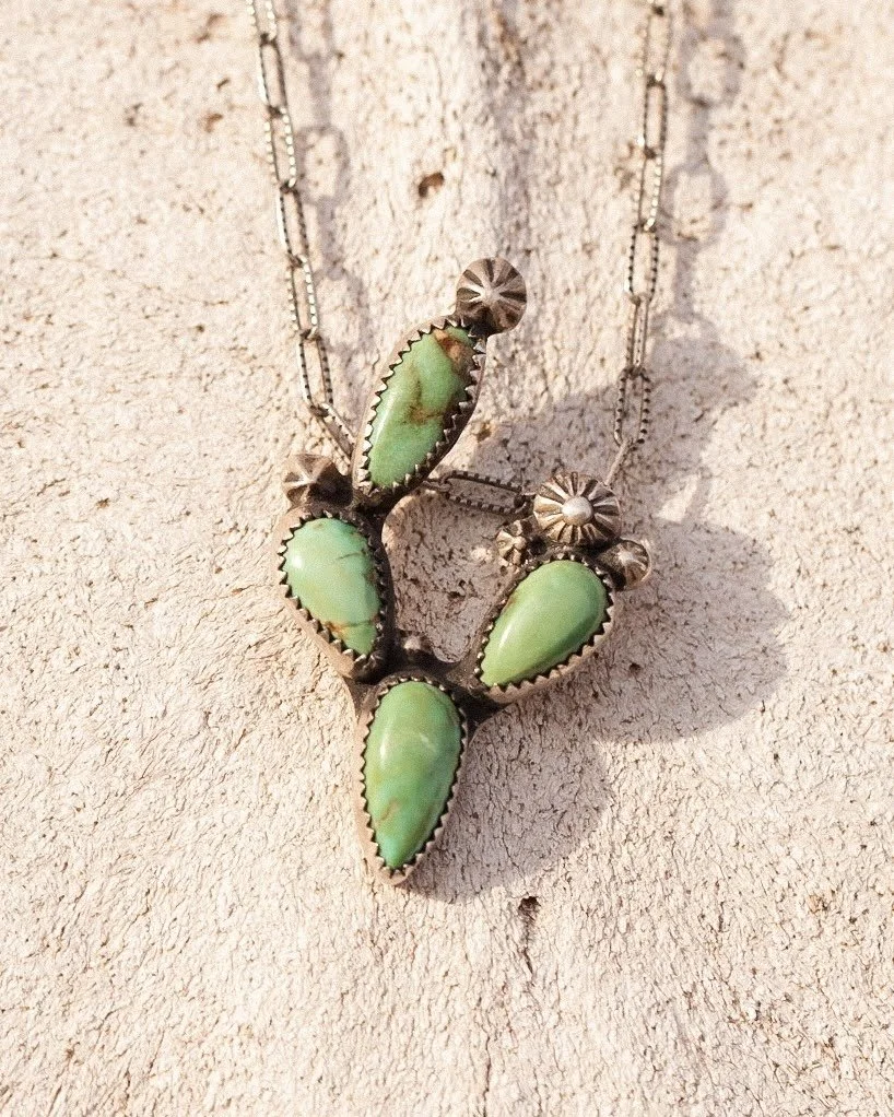 Sterling silver necklace with five green turquoise stones arranged in a cactus pattern on a textured beige surface.