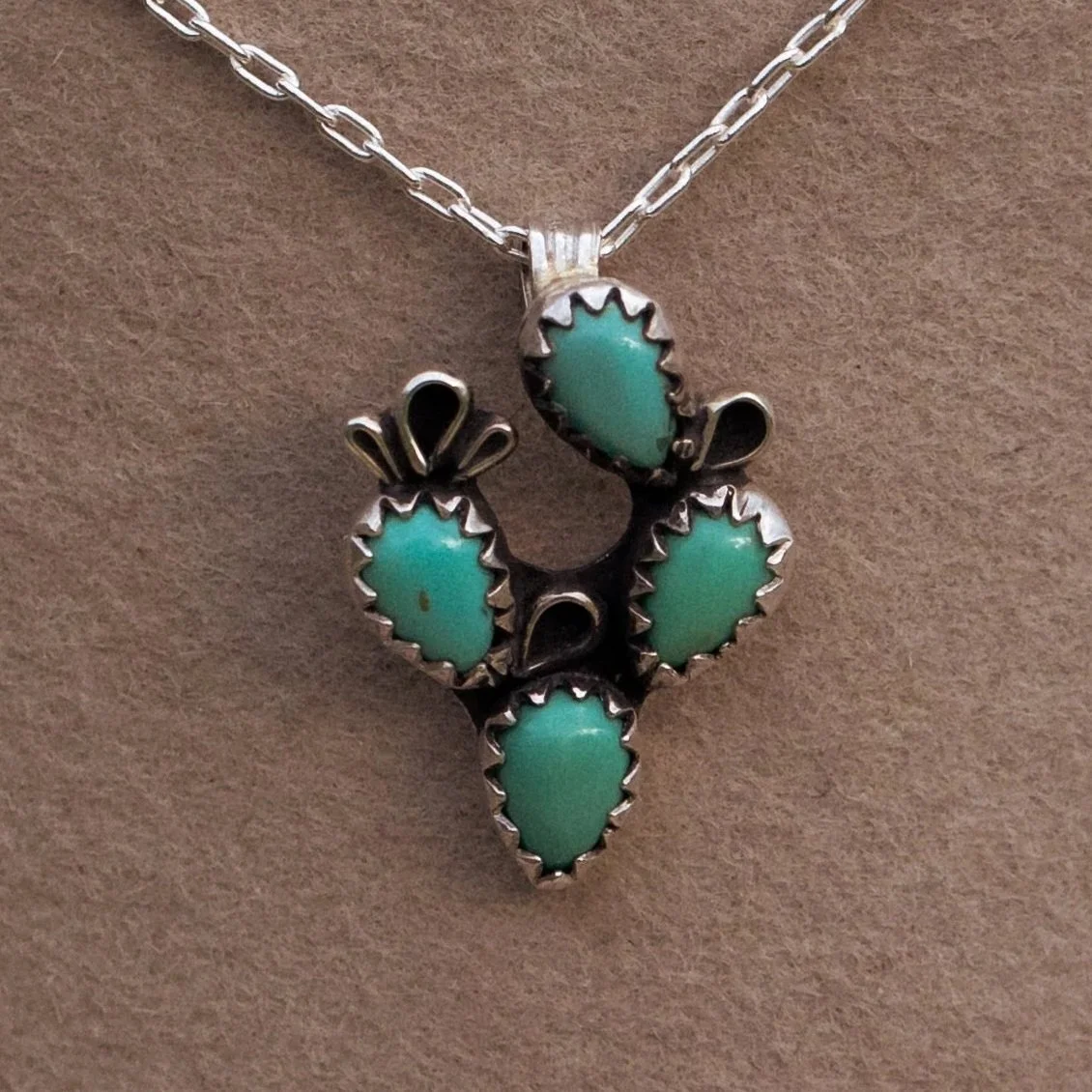 A sterling silver necklace with a pendant featuring five turquoise stones set in silver. Arranged in a cactus design.