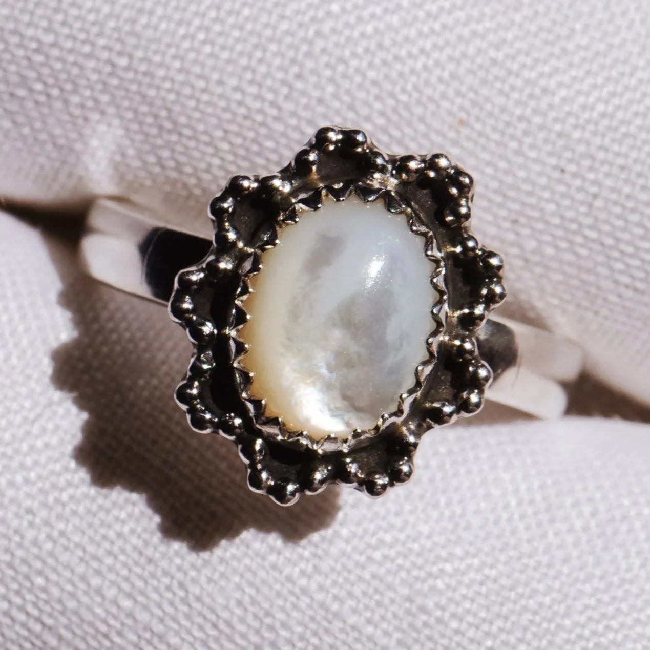 handmade sterling silver ring with mother of pearl stone set in a scalloped beaded wire border. faith has made