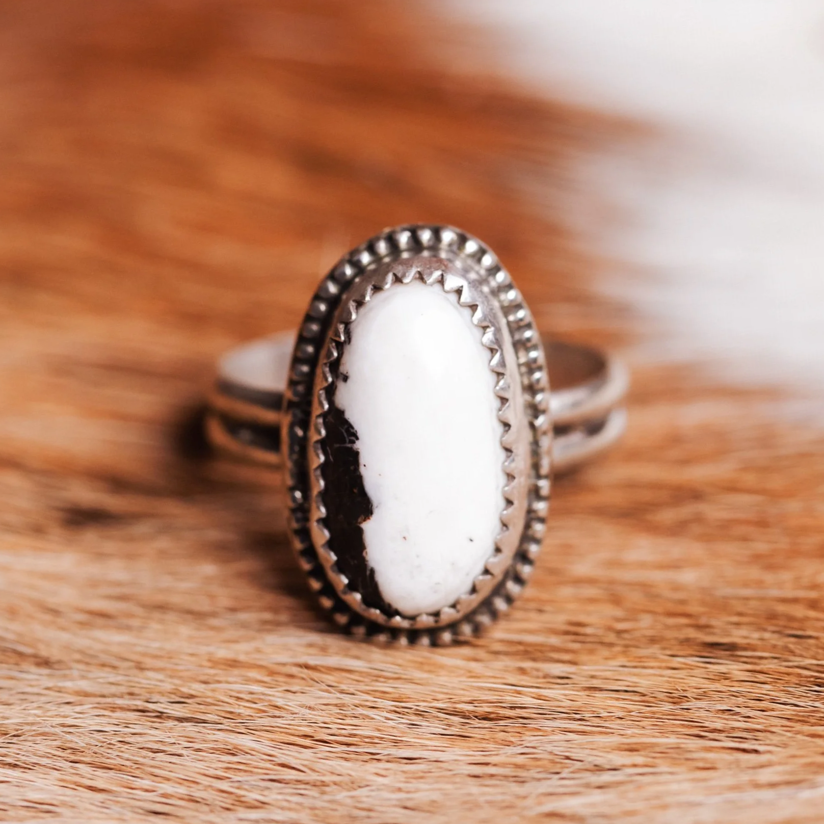 Silver ring with an elongated oval white buffalo stone on a cow hide.