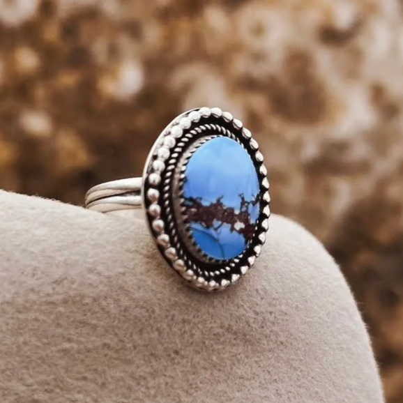 Sterling silver ring with an oval blue golden hills turquoise stone, set against a beige surface with a blurred brown background.