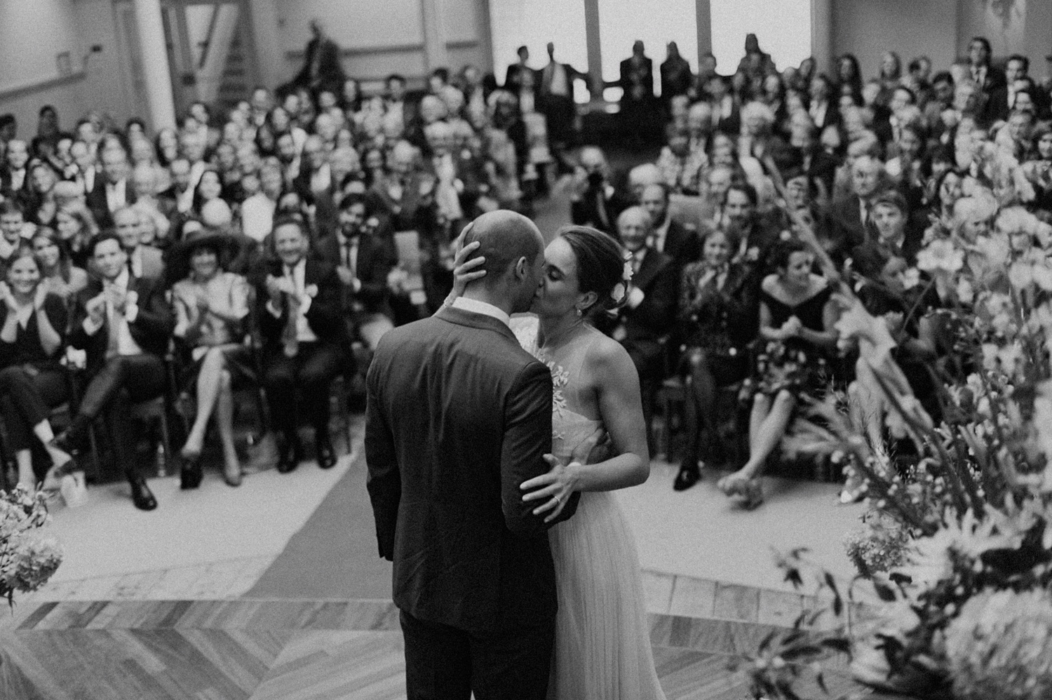 Bride and groom kissing wedding guests in the background at Keizersgracht Kerk Amsterdam