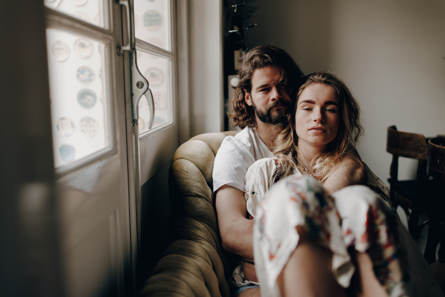 Couple sitting on couch facing the camera next to window