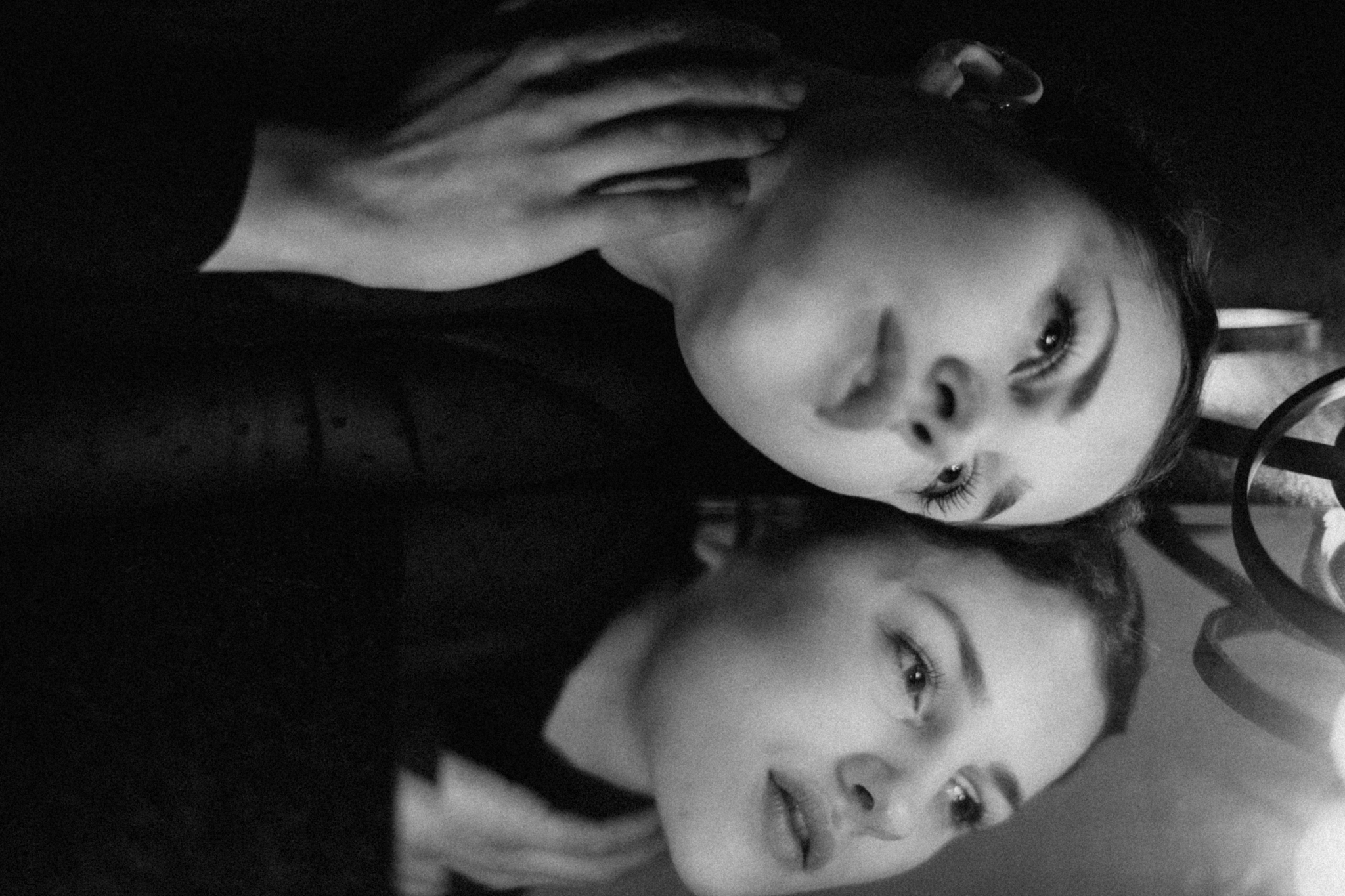 Black and white portrait of girl lying on mirror