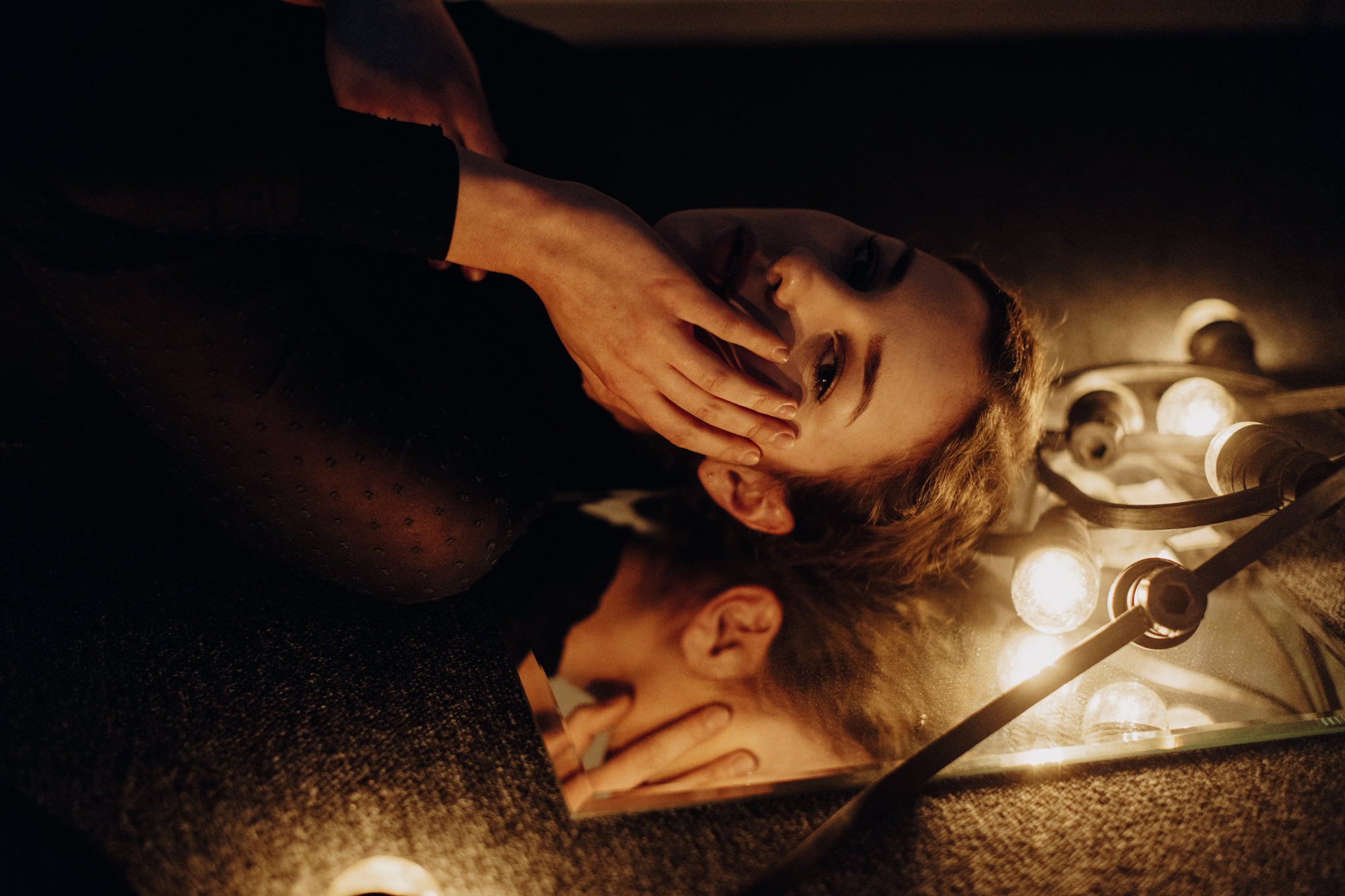 Girl lying on floor with face on mirror surrounded by string lights
