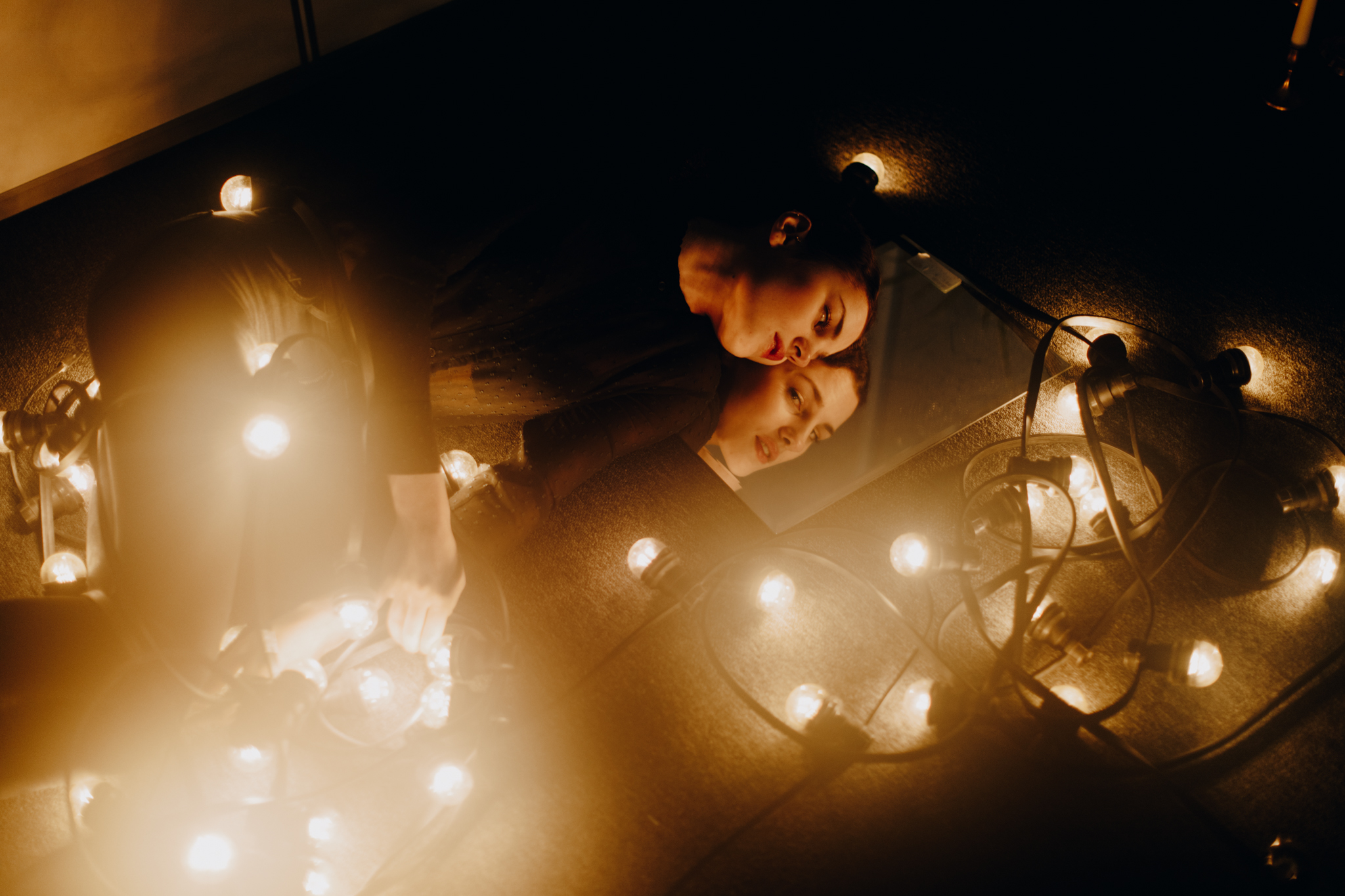 Girl looking in mirror surrounded by string lights