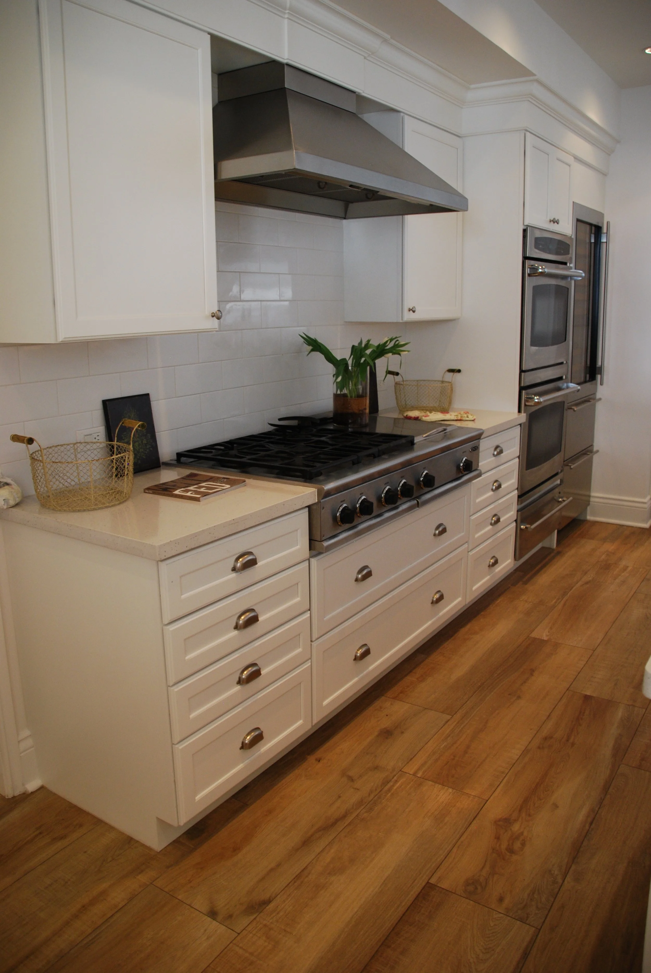White drawer cabinets around a stainless range and hood with stacked ovens at the end of the run
