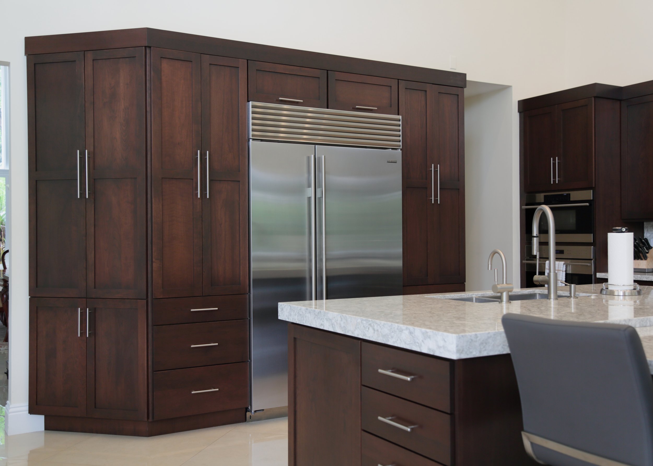 Stainless refrigerator framed by tall dark wood cabinetry with enclosed storage above and beside it