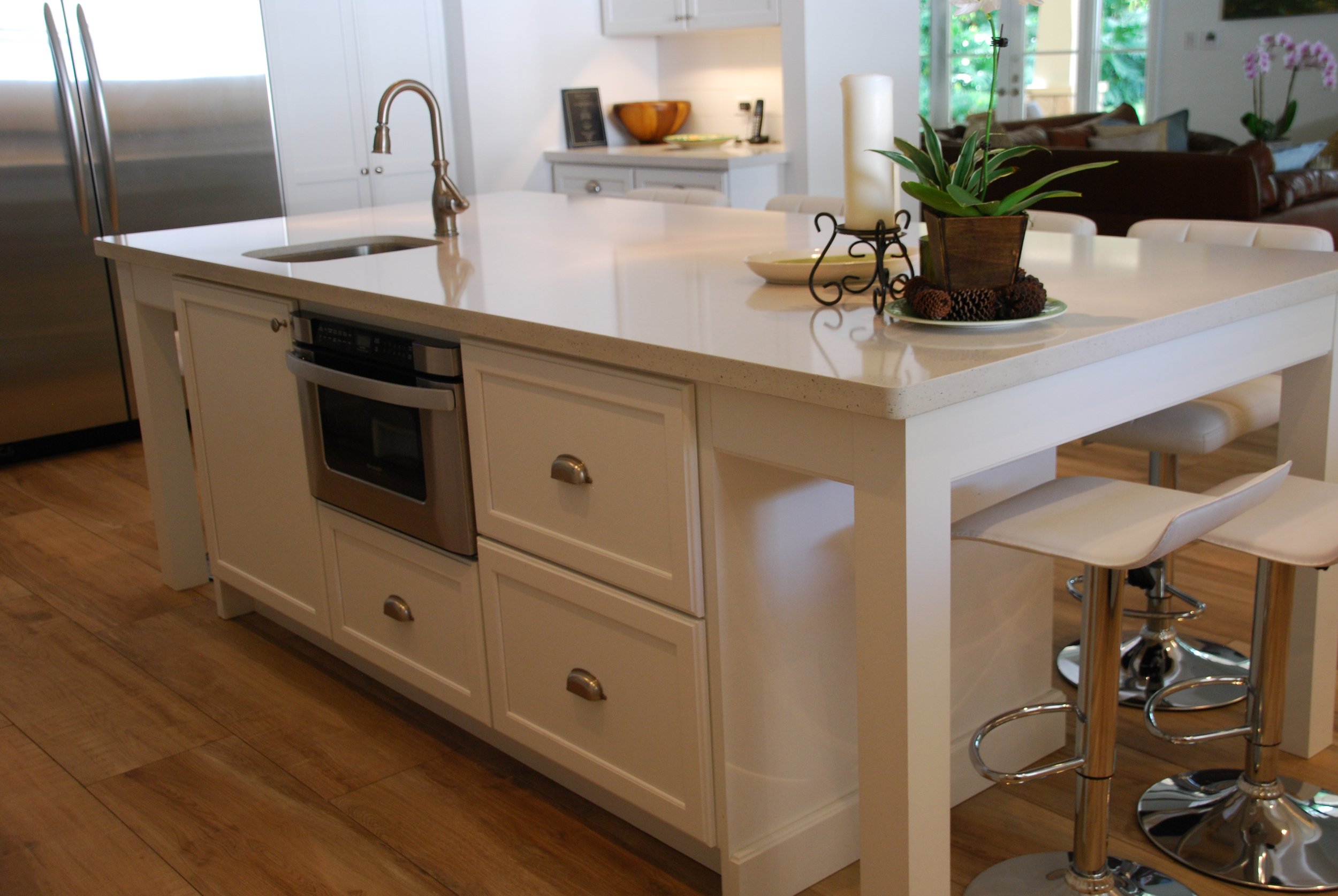 White island drawer cabinets and a built-in microwave beneath a light countertop with upholstered stools