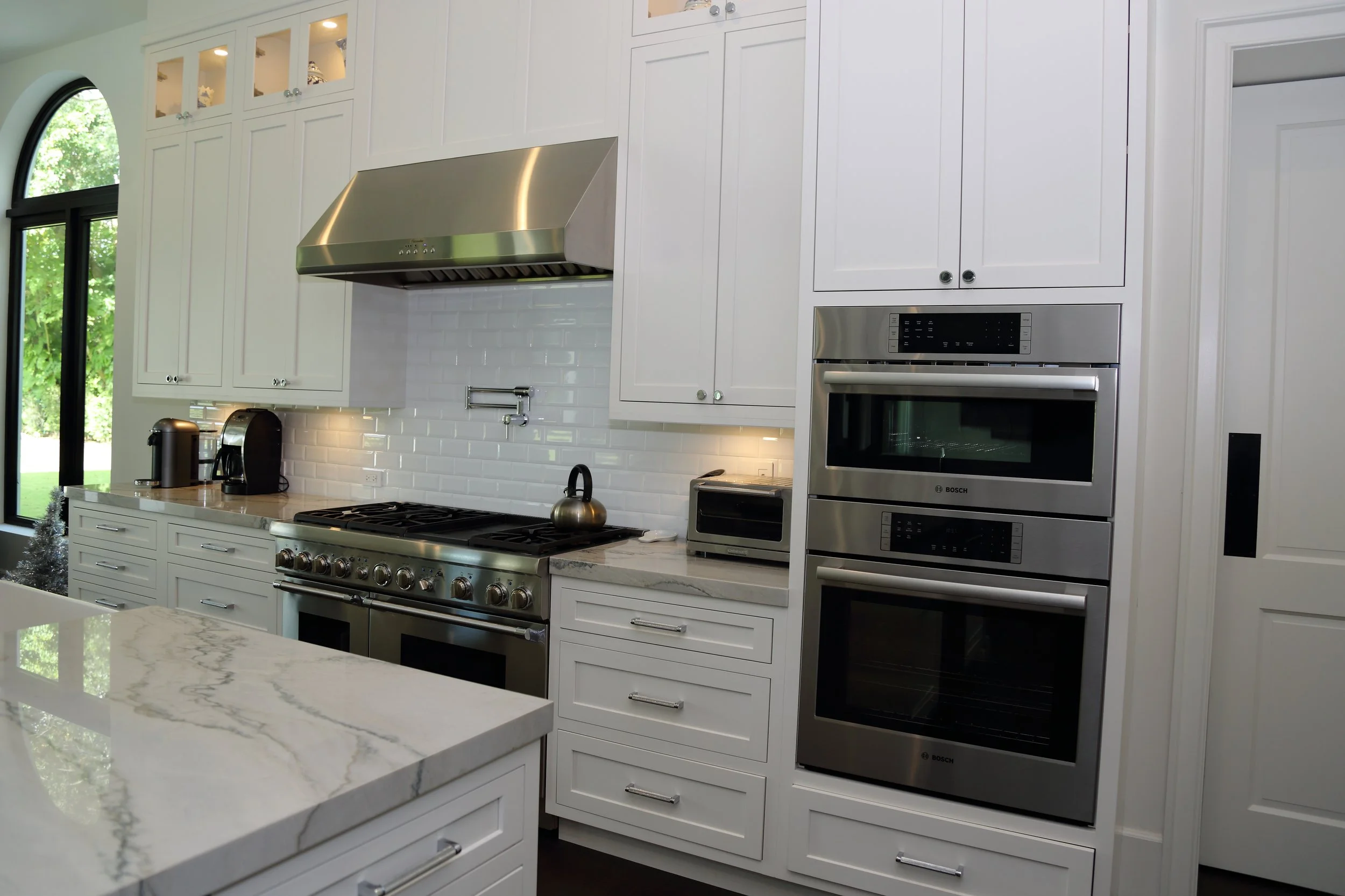 White kitchen cabinets surrounding stacked wall ovens beside the range and island