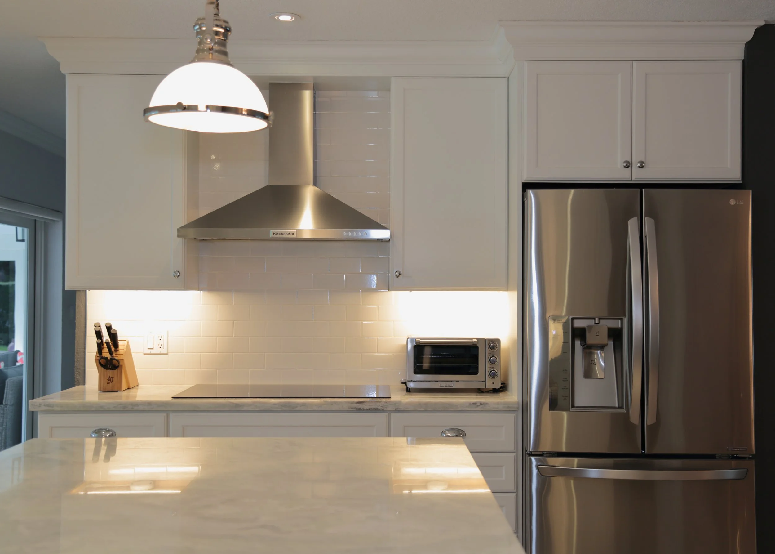 White upper cabinetry surrounding a stainless range hood beside a refrigerator and light backsplash