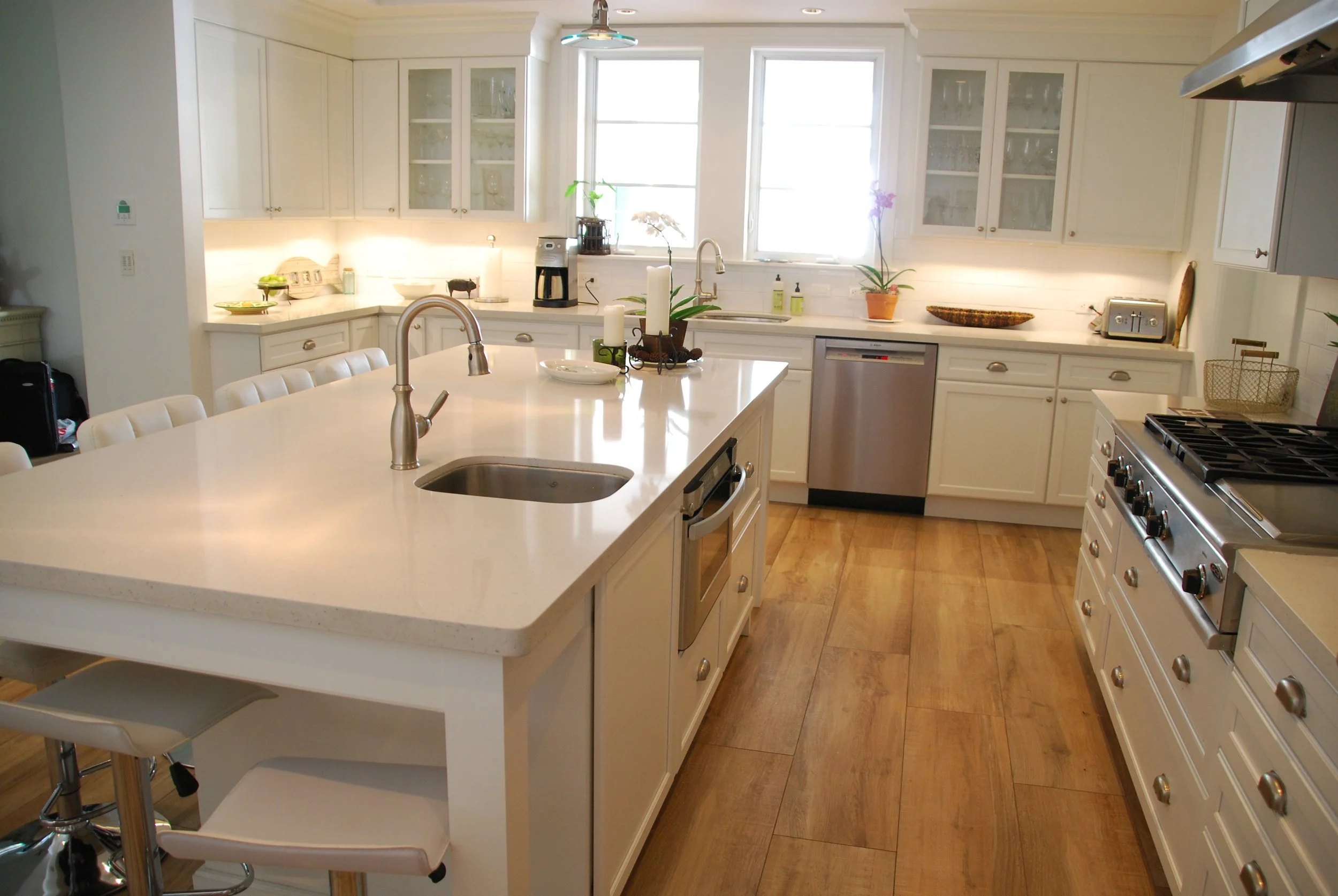 White kitchen island with a prep sink facing the window-side sink and perimeter cabinetry