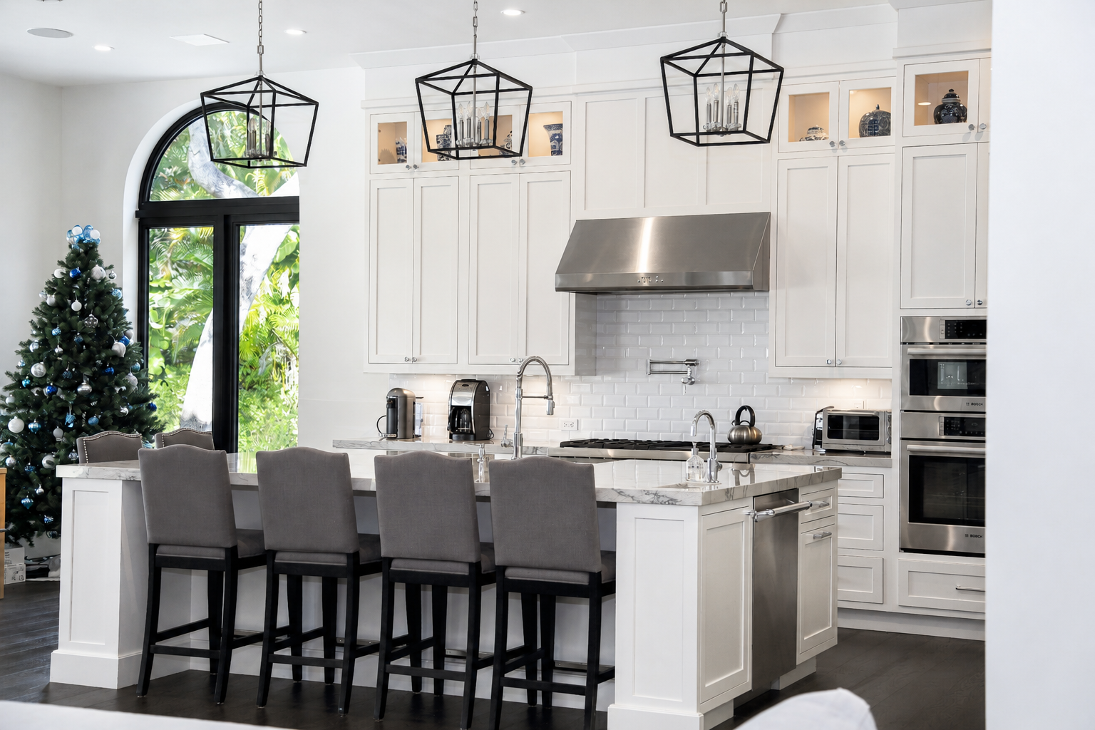 Jupiter kitchen with white custom cabinetry, a large island, black lantern pendants, and illuminated glass-front upper cabinets