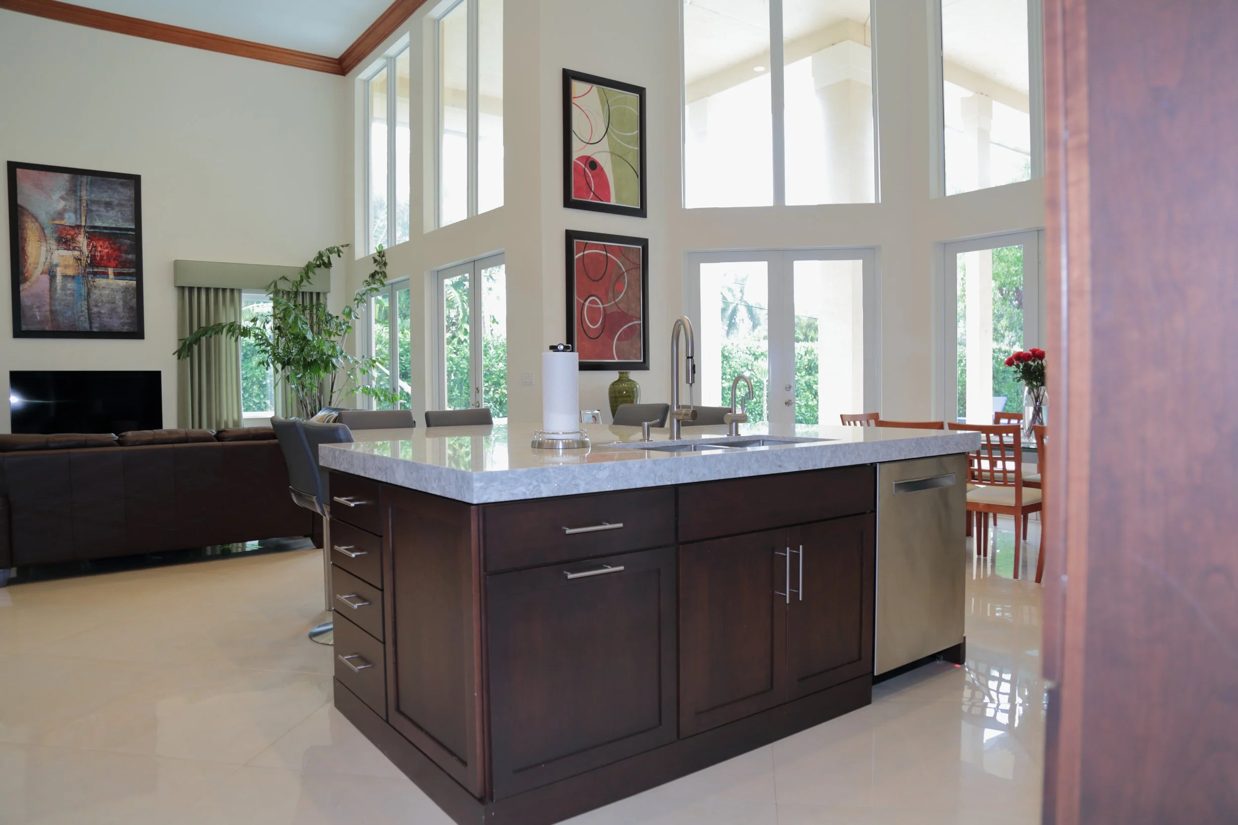 Dark wood kitchen island with paneled doors and drawers facing the bright open living area