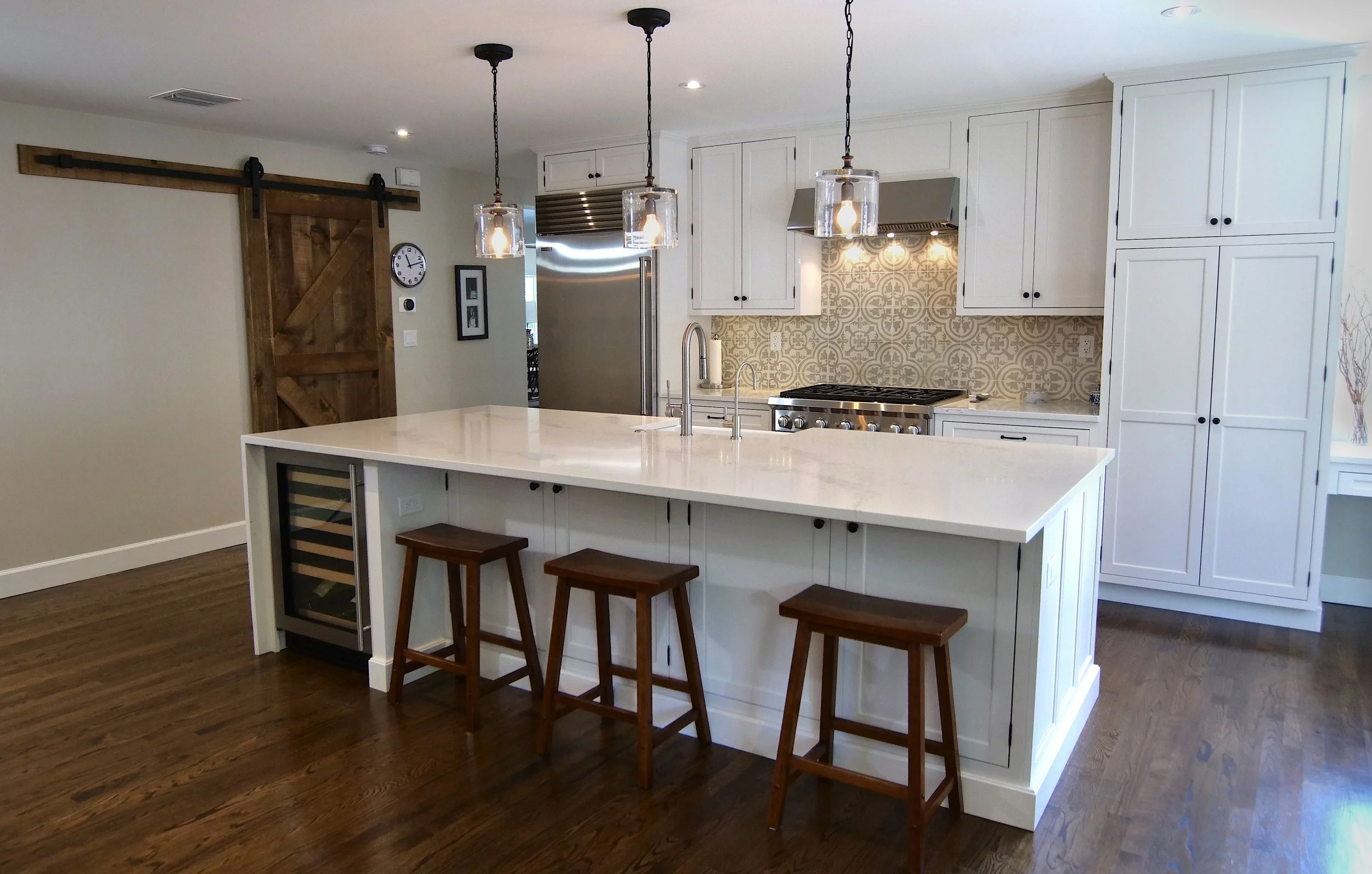 Tequesta kitchen with white custom cabinetry, a large island, wood stools, wine refrigeration, and glass pendant lights