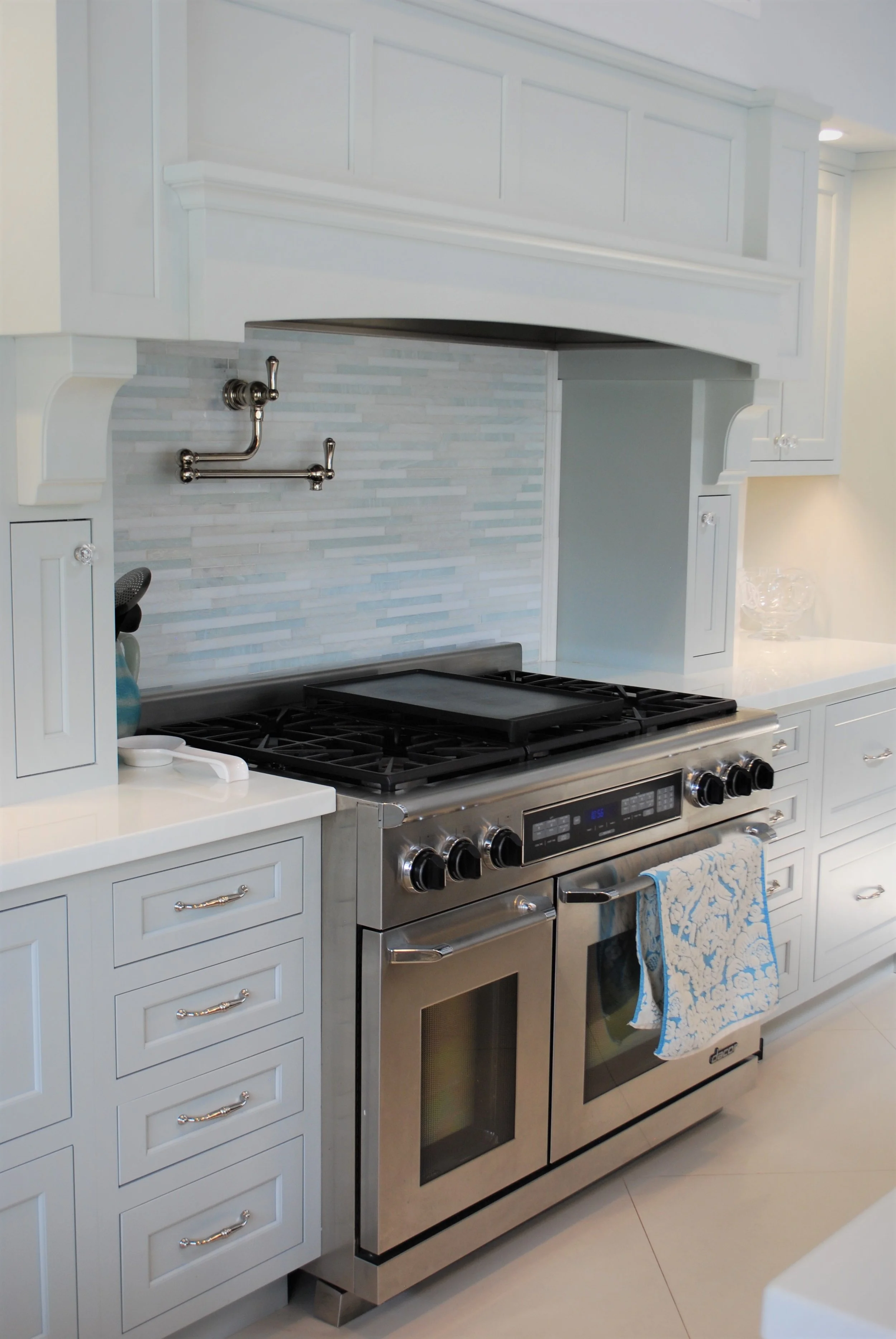 A modern kitchen with white cabinets, a stainless steel gas stove, and a tile backsplash. There are towels hanging on the oven handle.