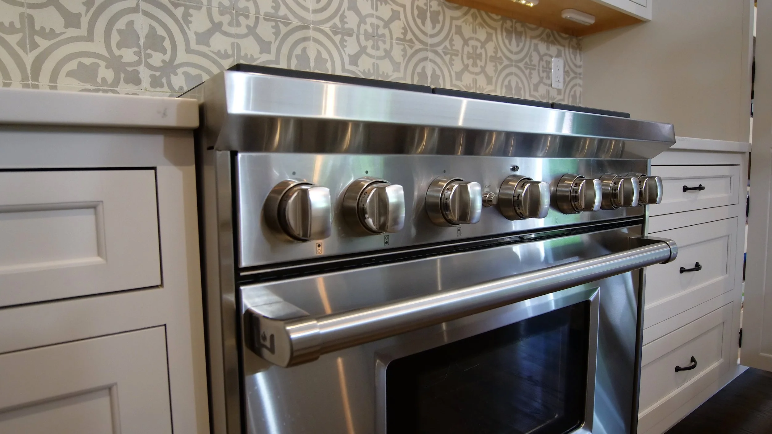 White kitchen drawer cabinetry beside a stainless range and patterned backsplash