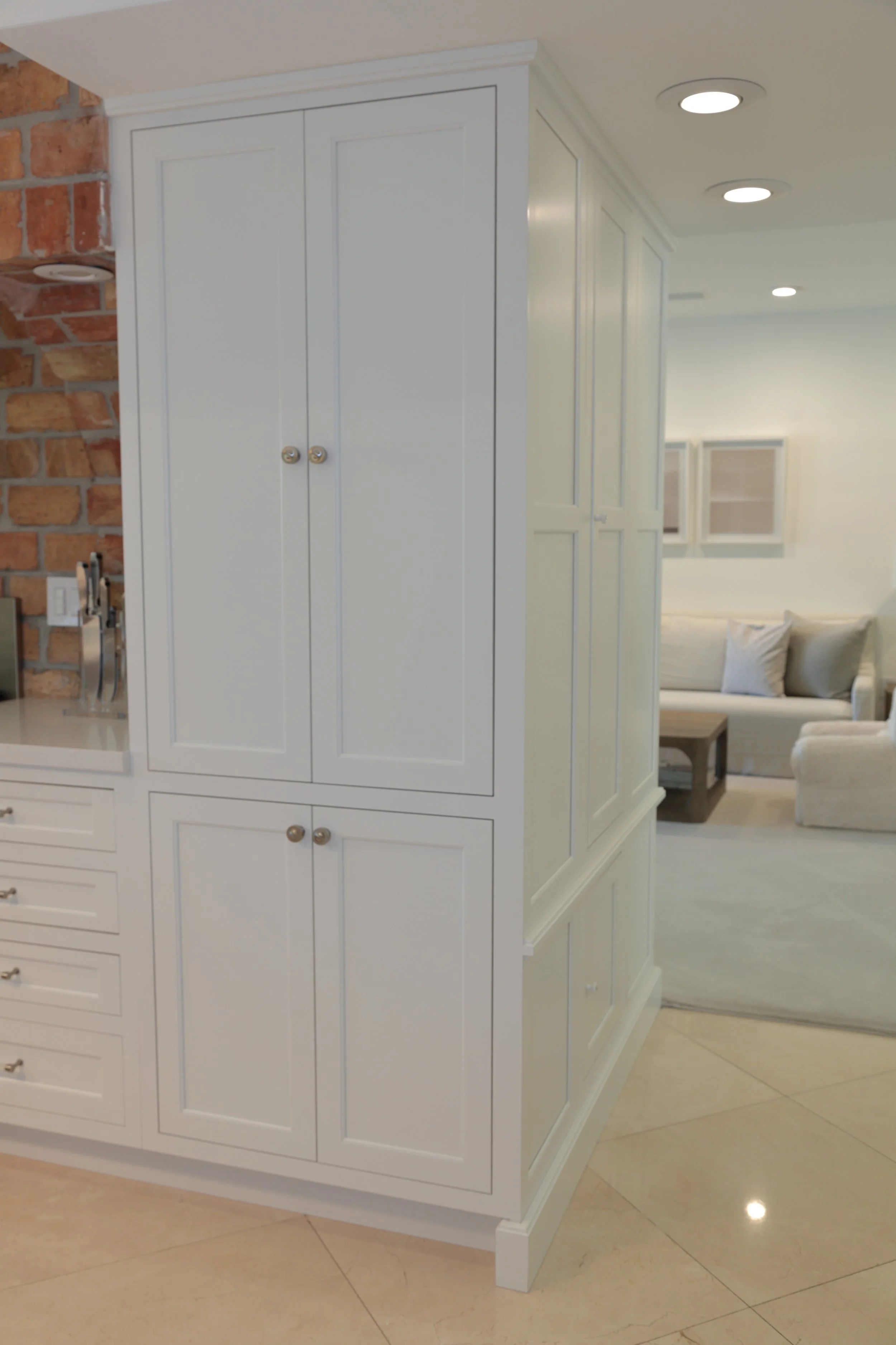 Tall white pantry cabinets with paneled fronts and crown molding beside the brick cooking alcove