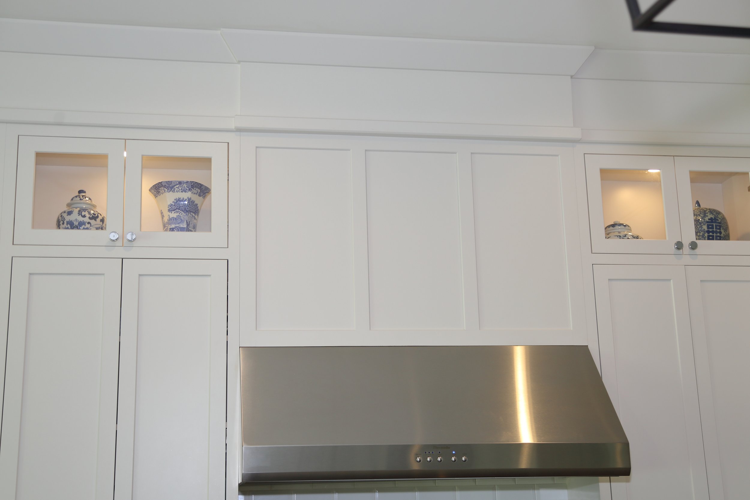Illuminated glass-front display cabinets above tall white cabinetry and a stainless range hood