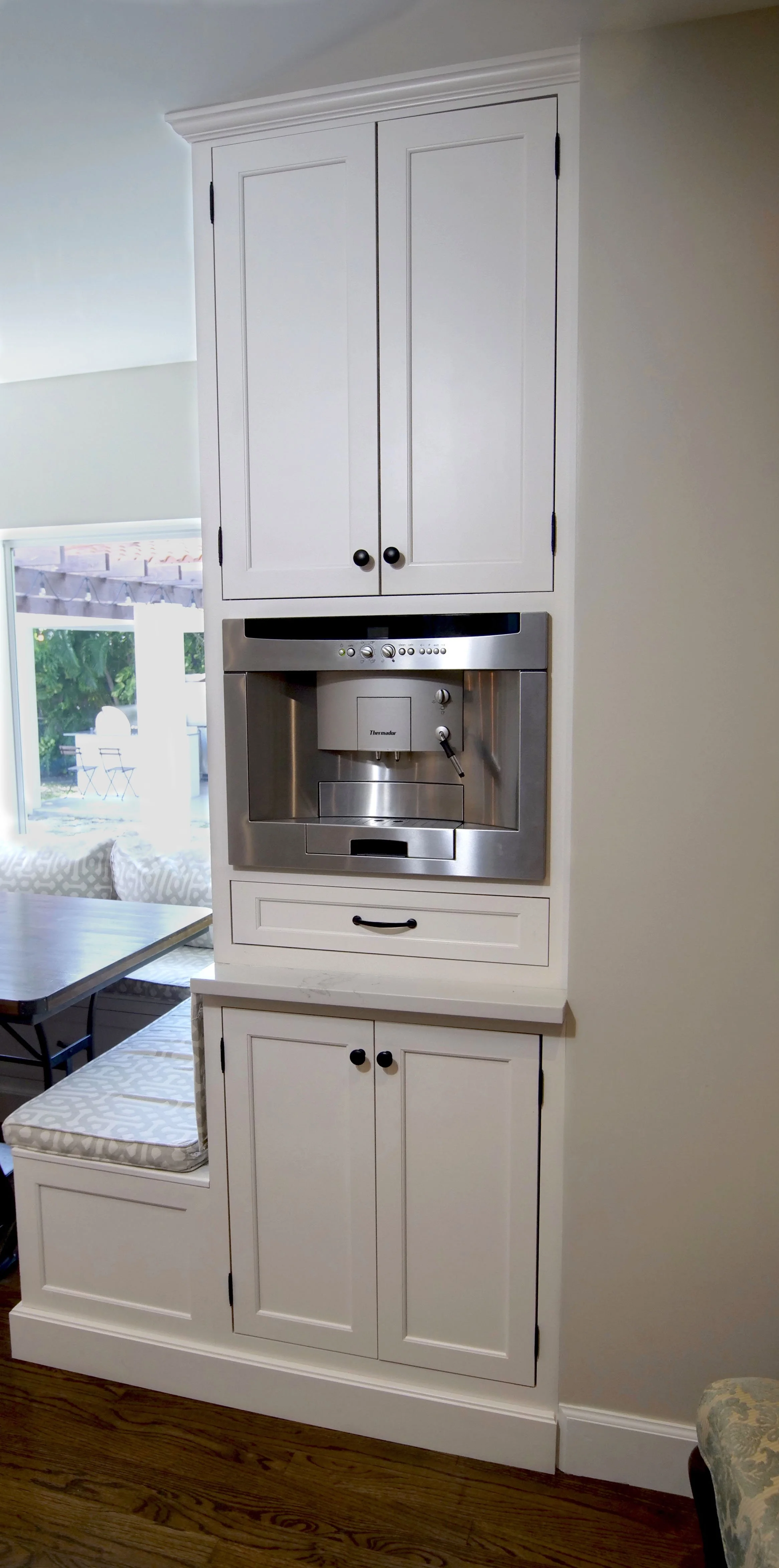 Tall white custom cabinet with a built-in coffee machine, drawer storage, and enclosed cabinets