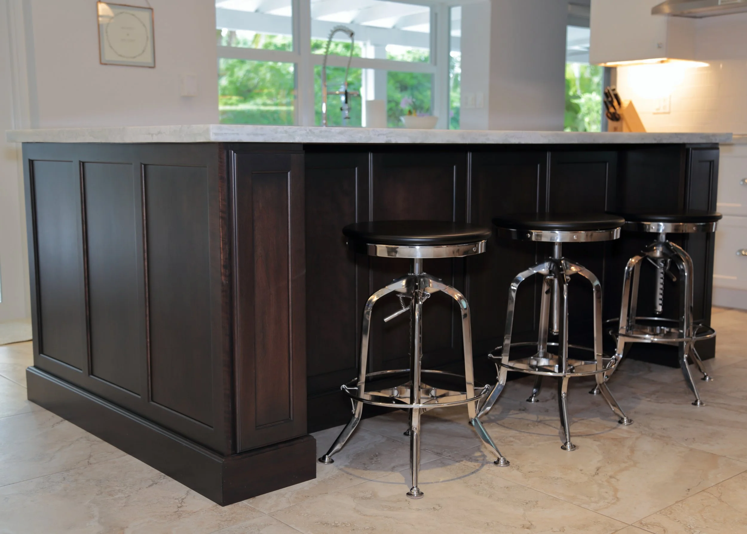 Dark wood kitchen island with paneled ends, a light countertop, and metal-framed counter stools