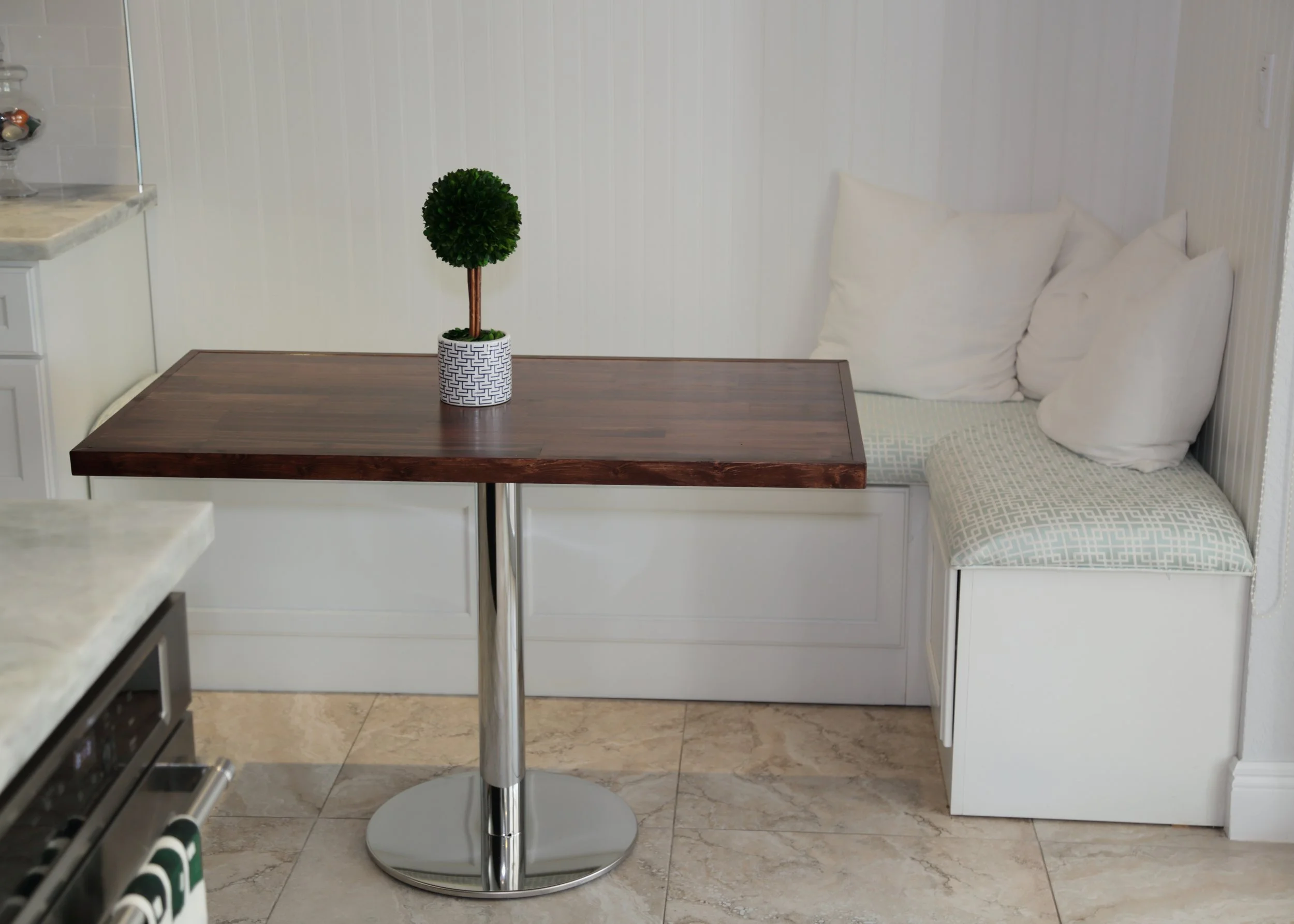 White built-in breakfast nook with cushioned bench seating and a wood table beside the beverage station