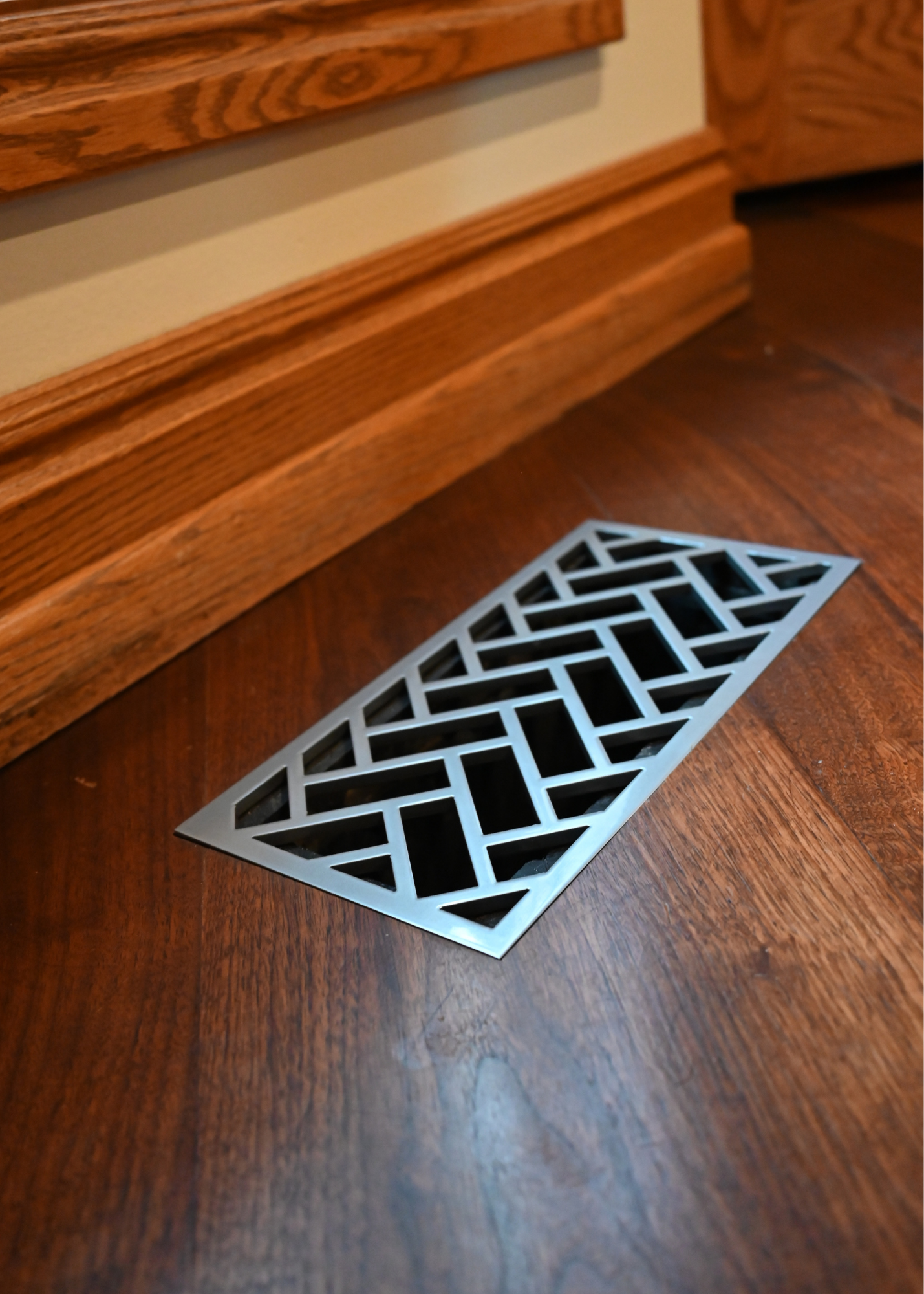 Steel flush mount grill in a hardwood floor. This is the herringbone design in a gloss silver powder coat.