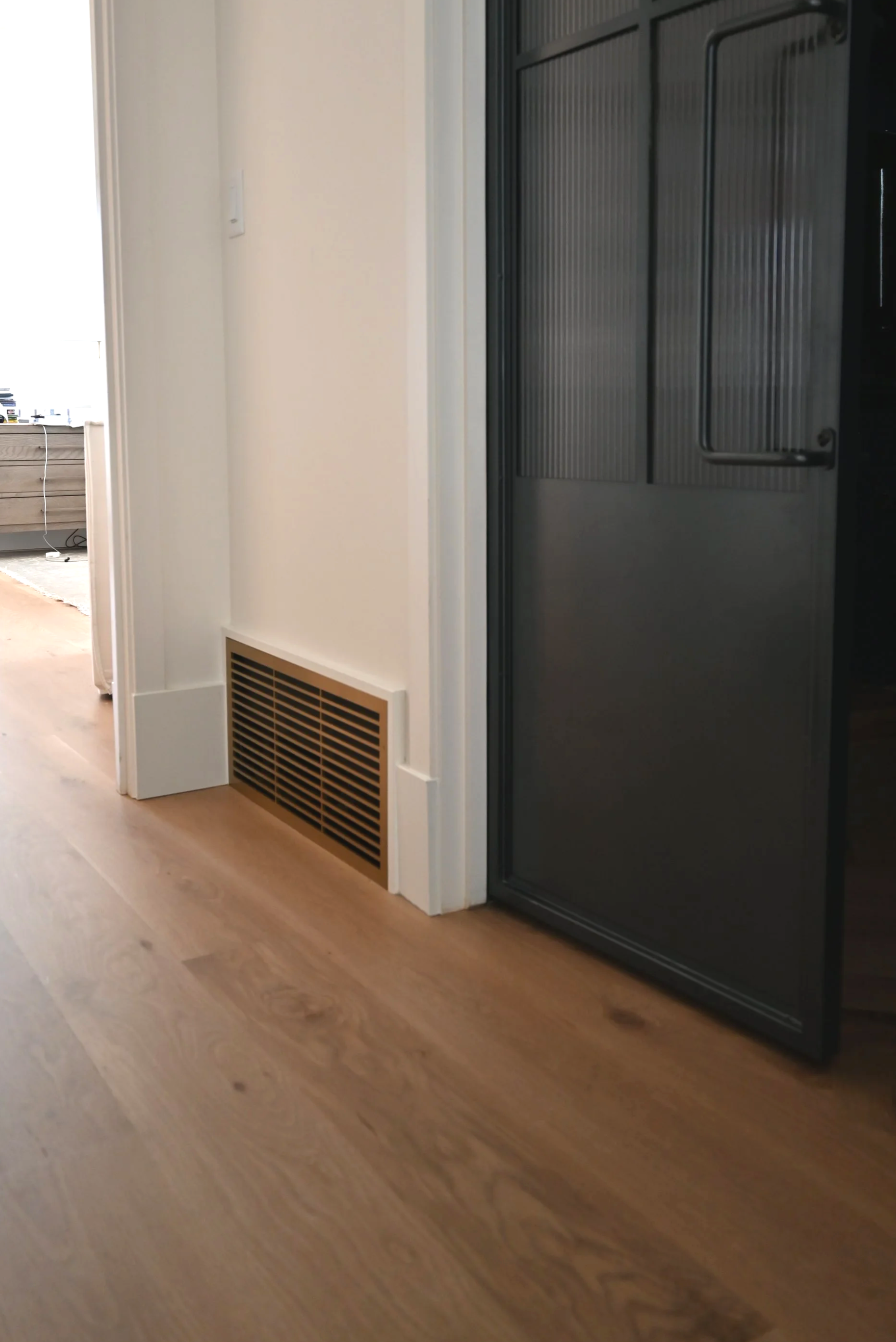 Decorative hallway air return grill in a vintage gold color next to a heavy black steel door. 