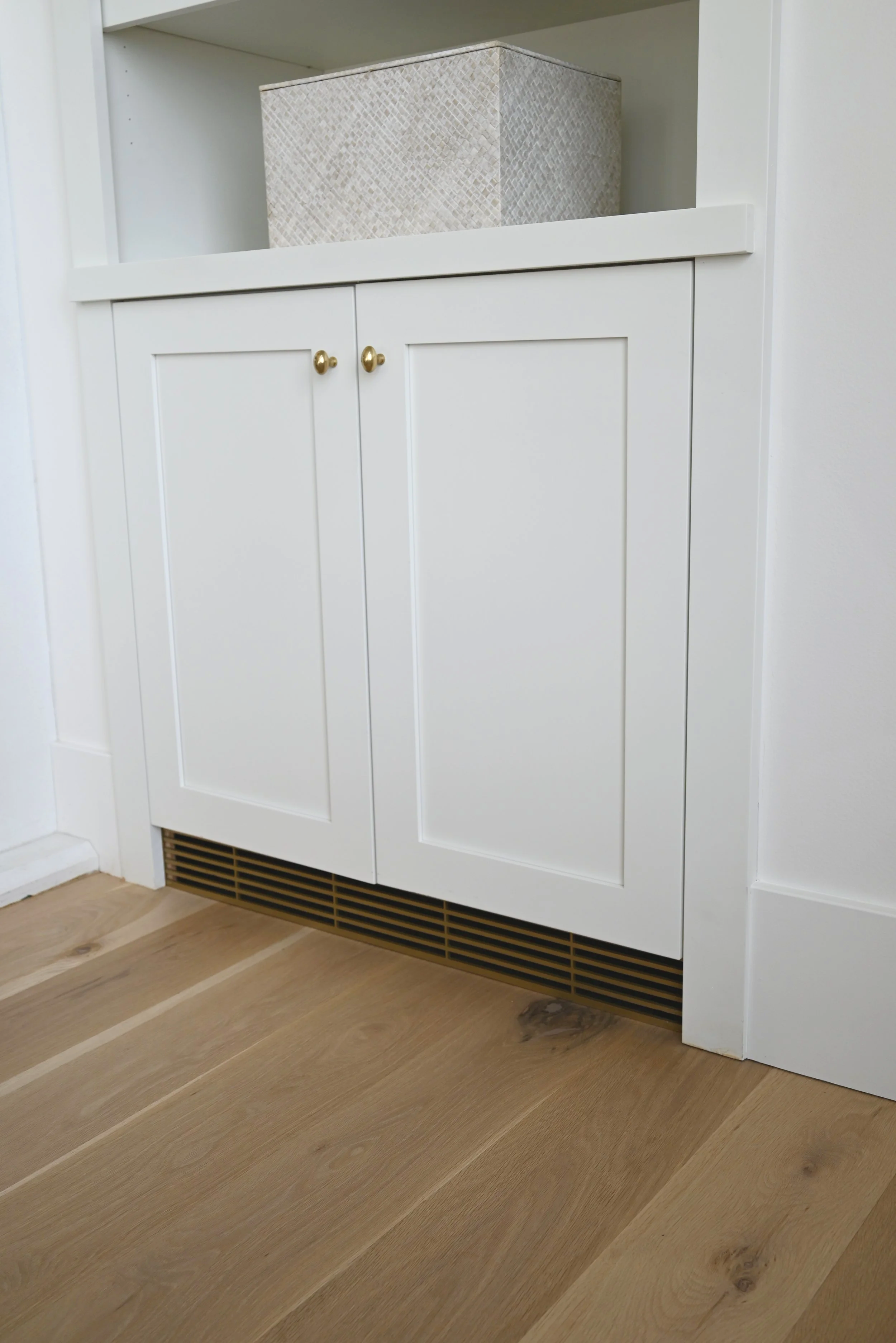 Custom metal toe kick return air vent located under a cabinet spanning across the whole surface of the toe kick.