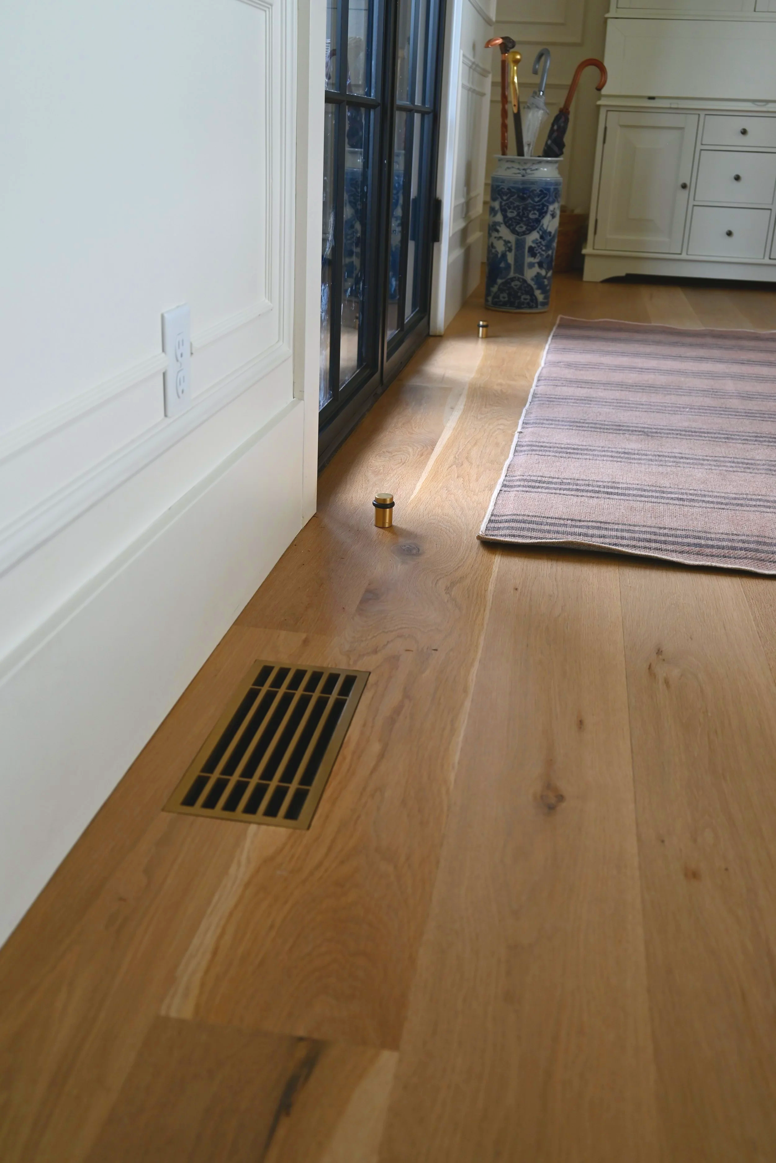 Decorative steel floor vent that is flush mounted in a beautiful entry way with a heavy steel front door. 