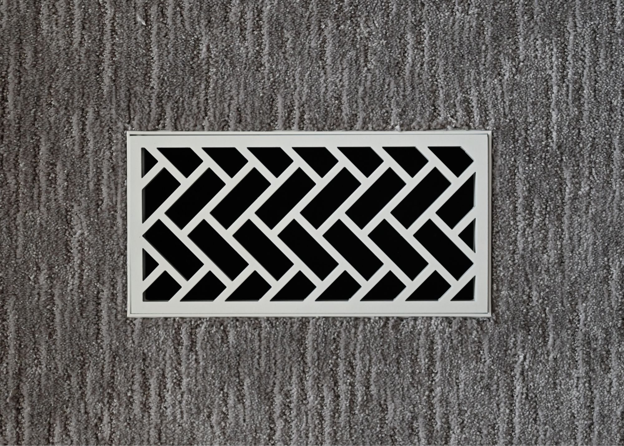 Steel flush mount vent installed into carpet. This decorative metal grill is in our herringbone designed and is powder coated textured white. 