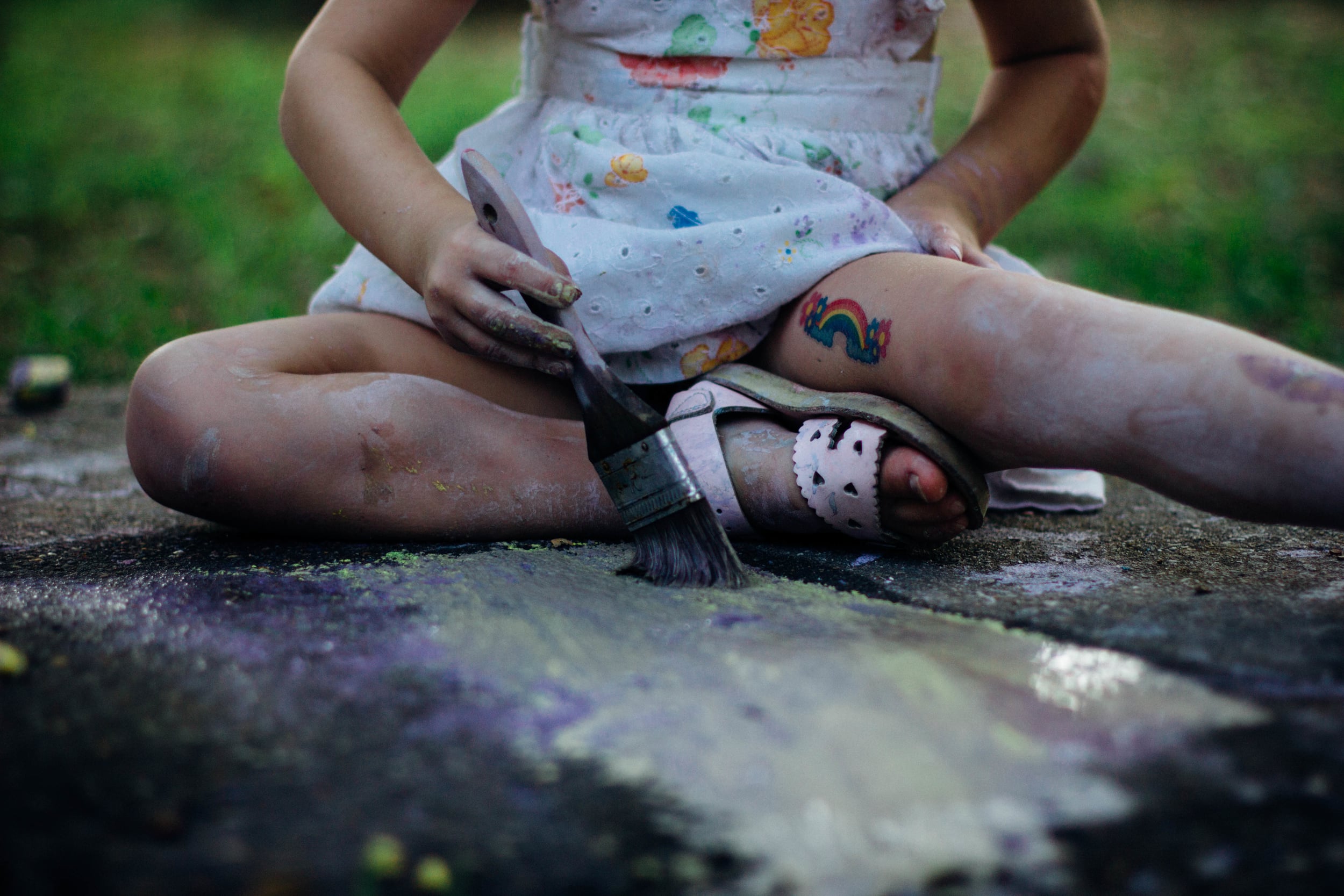 girl painting on a sidewalk with a rainbow tattoo