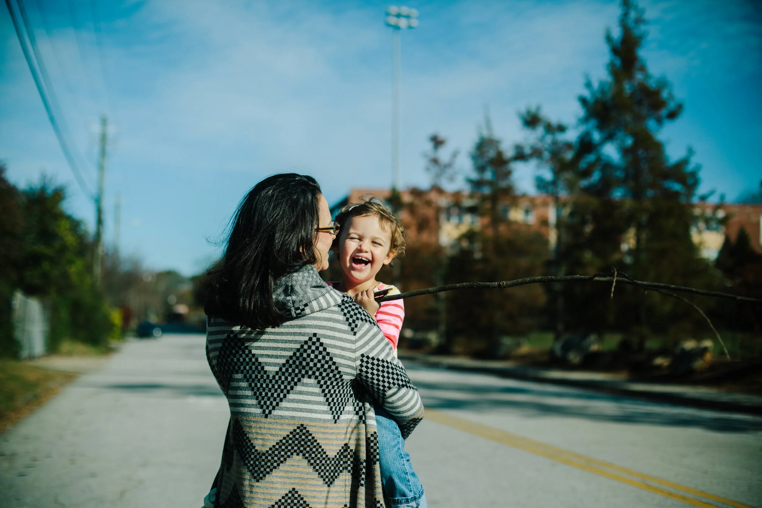 mother holding daughter who is laughing and carrying a stick during a family documentary photography session in atlanta