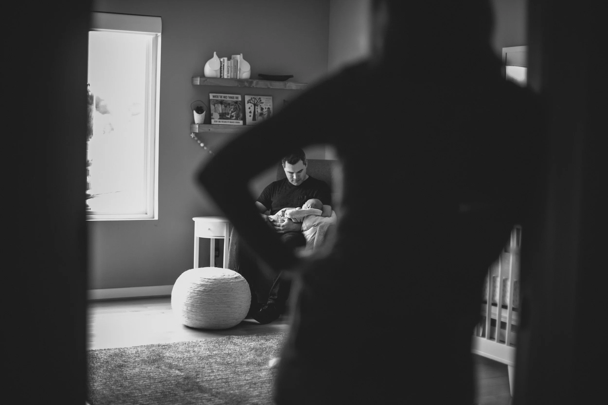 woman in doorframe looking at father holding newborn daughter from newborn family documentary photography session in atlanta