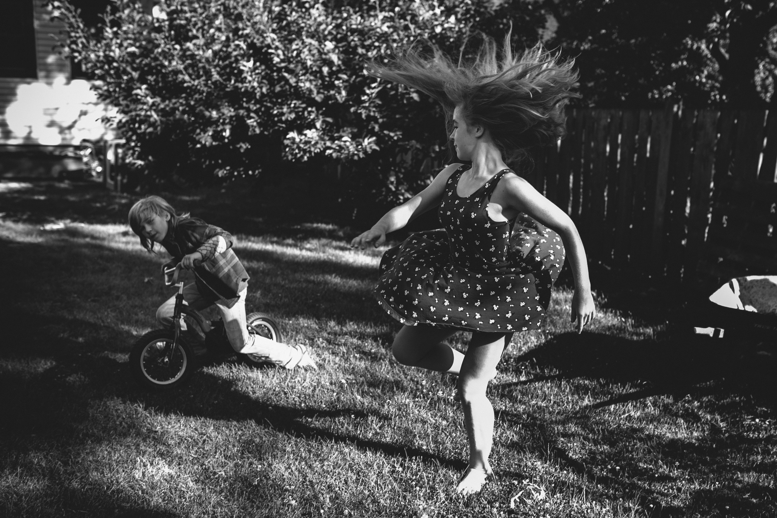 Girl spinning with hair flying while boy on a bike looks on from portrait of play photography session