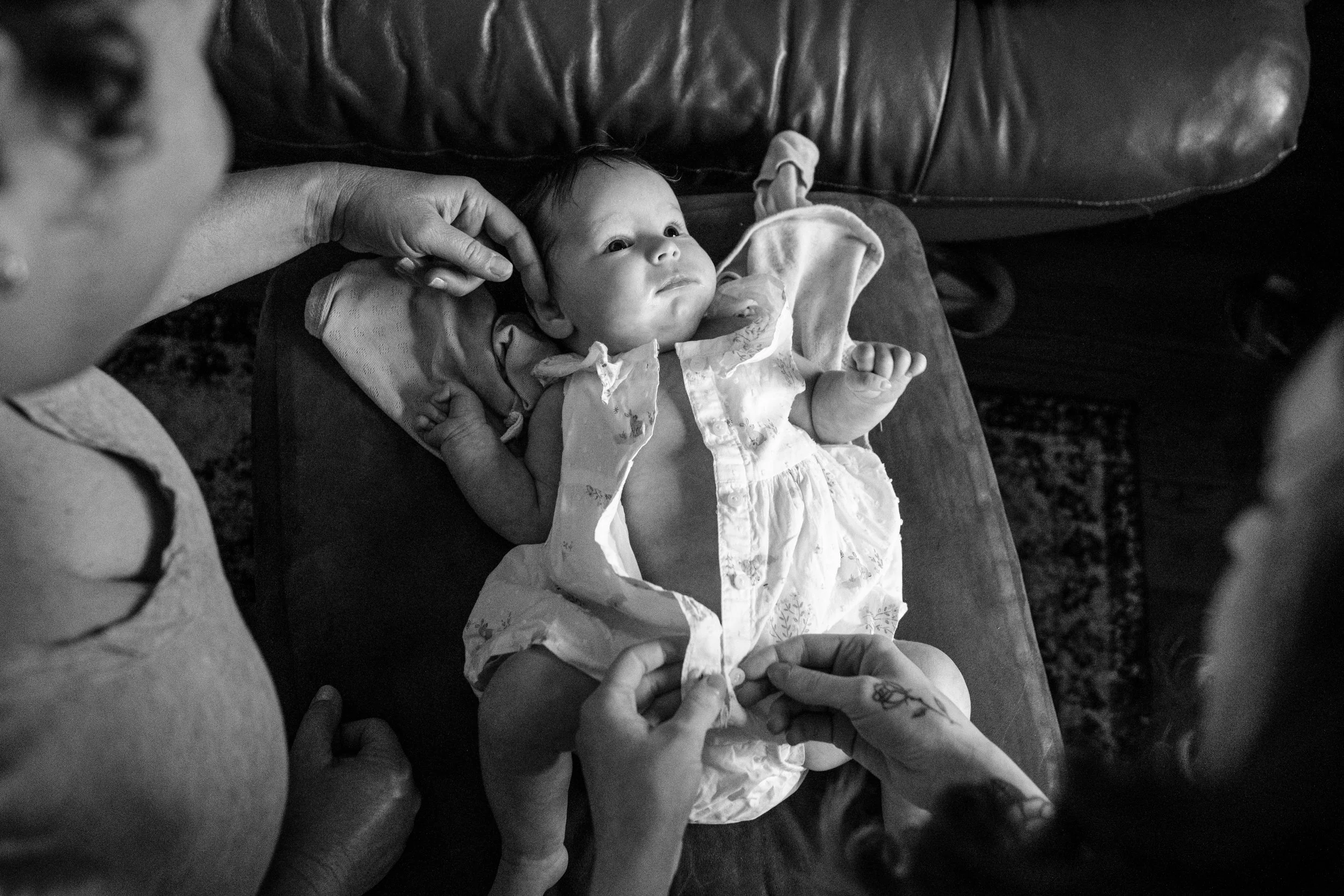 a black and white photo from above of a grandmother touching the cheek of a baby while the mother buttons her outfit