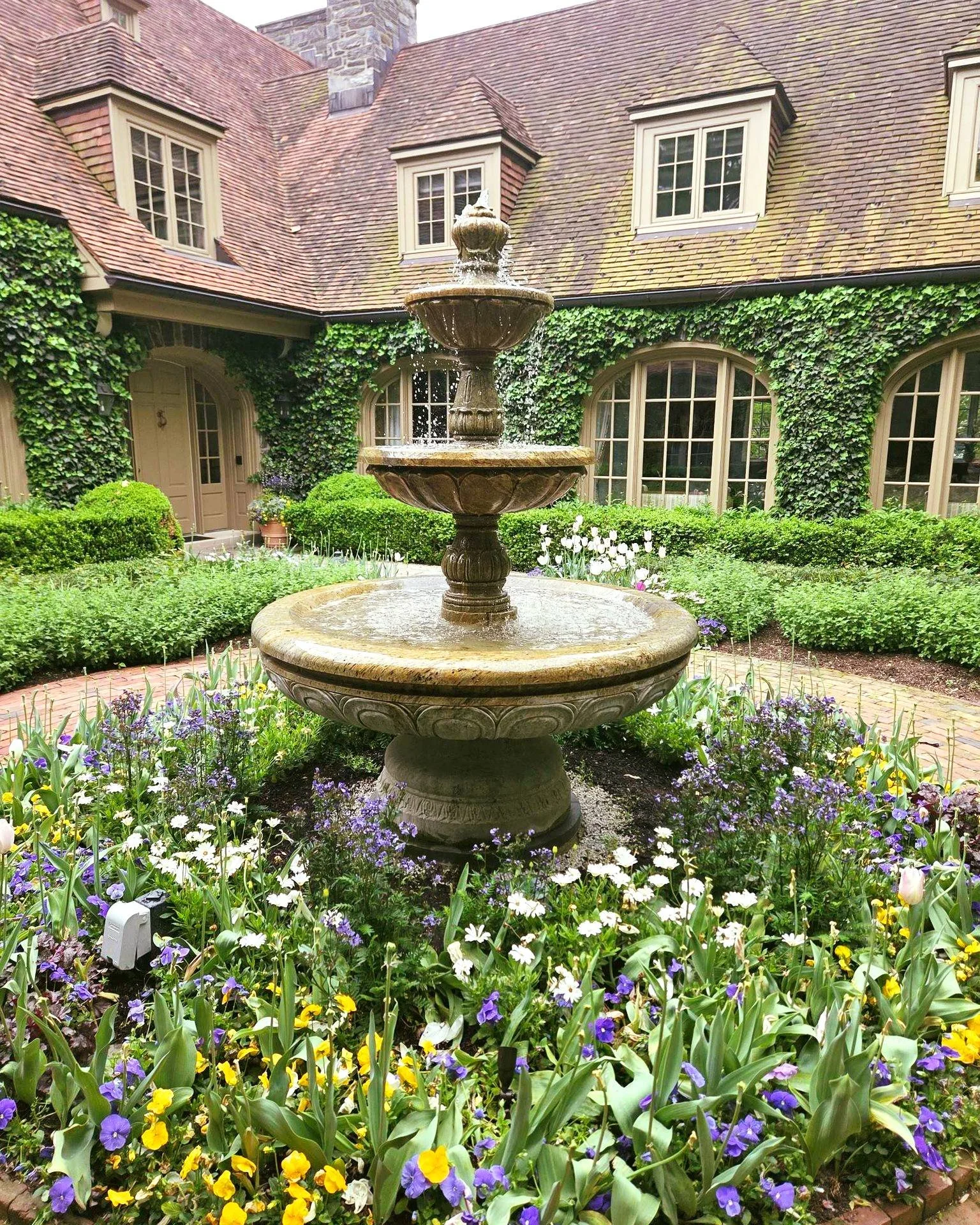 🌸 10 years later &mdash; still flowing beautifully.
This courtyard fountain is one of our favorite installations, and spring makes it absolutely come alive. Pansies, tulips, ivy-draped walls, and the sound of water cascading through three tiers of s