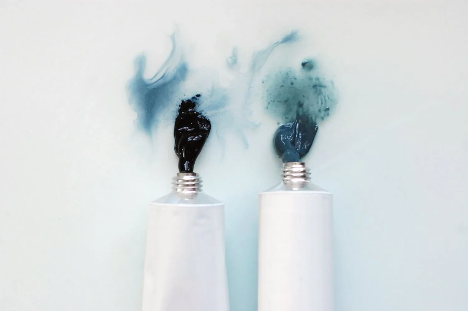 two blobs of blue paint extruding from white metal paint tubes onto a white surface