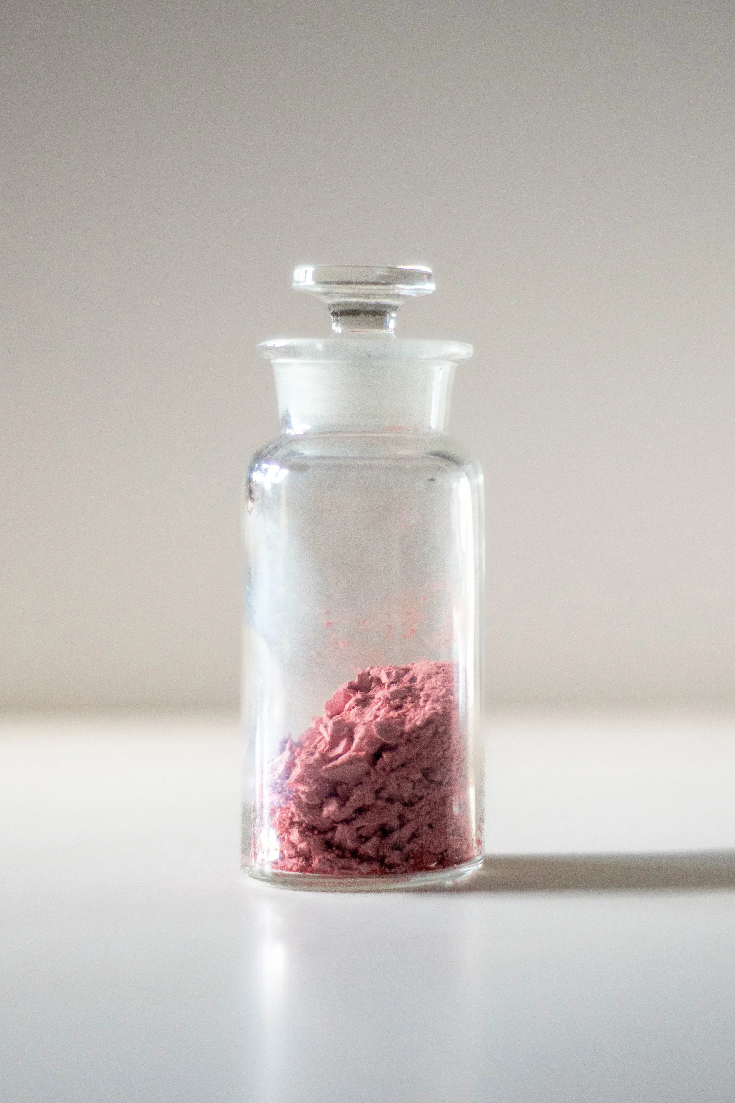 a stoppered glass bottle of of pink granules on a white surface