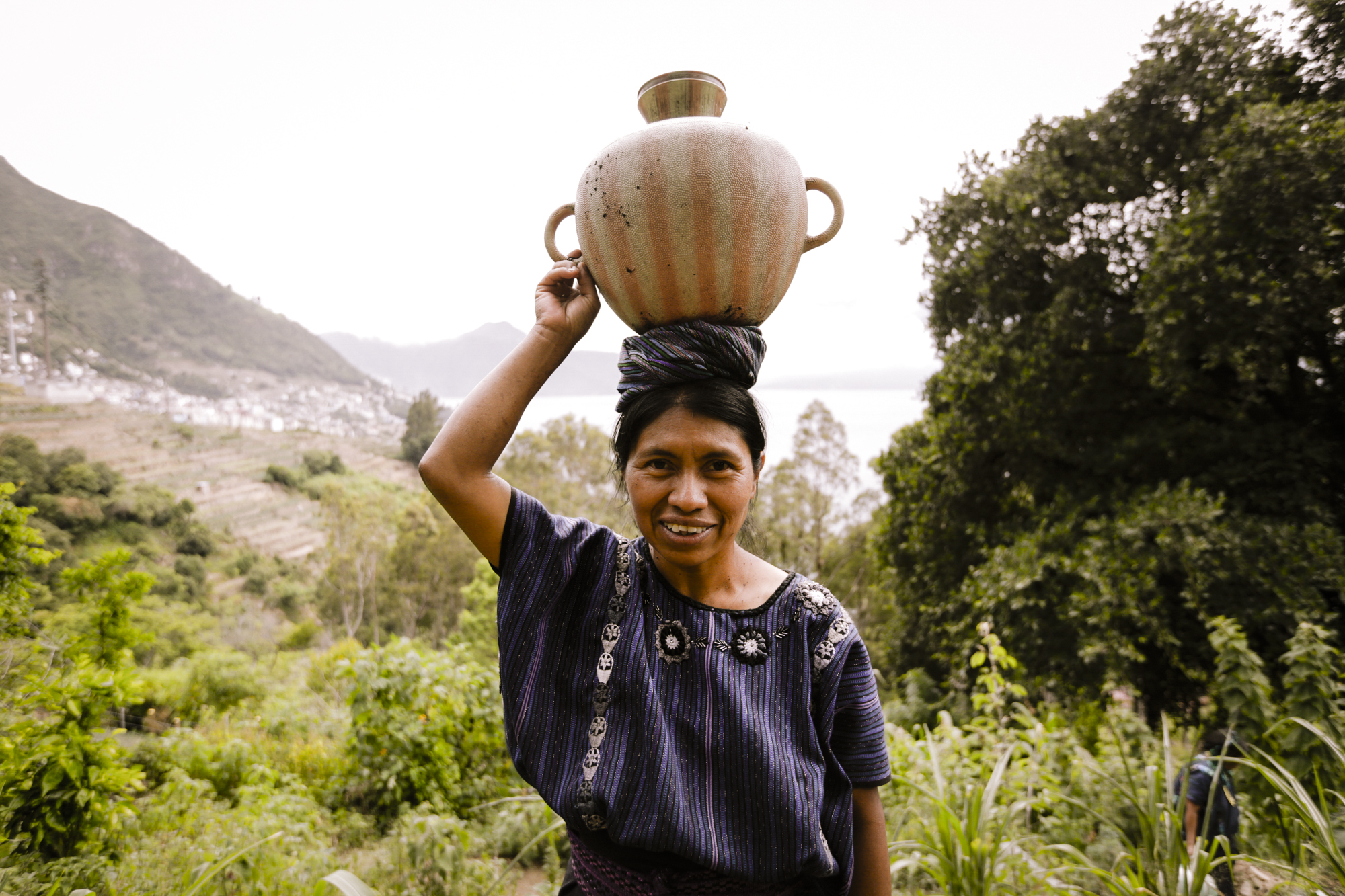 A woman carries a bucket of water on her head as she helps take care of plants in a community garden in San Antonio Palopó, Guatemala, in August 2018. The community garden in San Antonio helps provide food and jobs for indigenous people that live in this area.