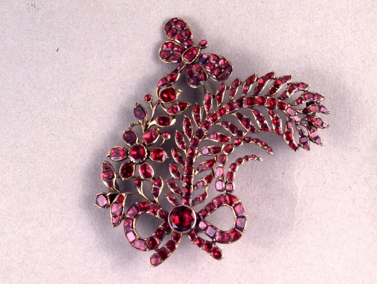 England, c. 1726-1775 Aigrette in the form of flowers and a feather tied with a bow and with a trembler butterfly. Gold with a dished closed-back and set with flat-cut garnets. British Museum