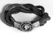 Bracelet of four hollow chains of woven and plaited hair twisted together and terminating in engraved gilt mounts and a clasp of a wheel-like openwork gilt roundel set with a Canadian ten-cent piece of 1871 and decorated on the front with blue enamel. British Museum.