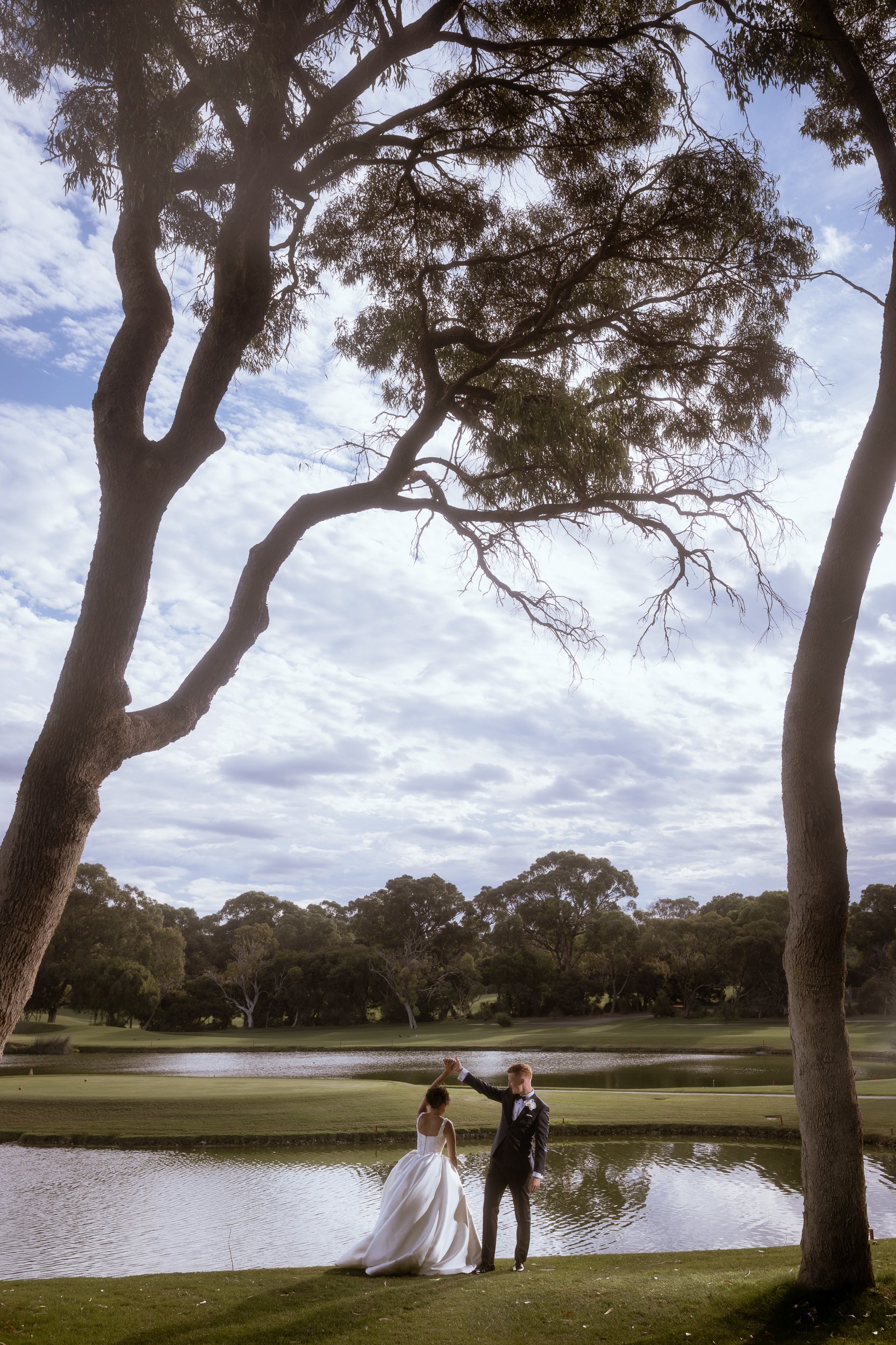 Groom spinning his bride beside a tranquil lake framed by sweeping gum trees, captured by a Perth wedding photographer.