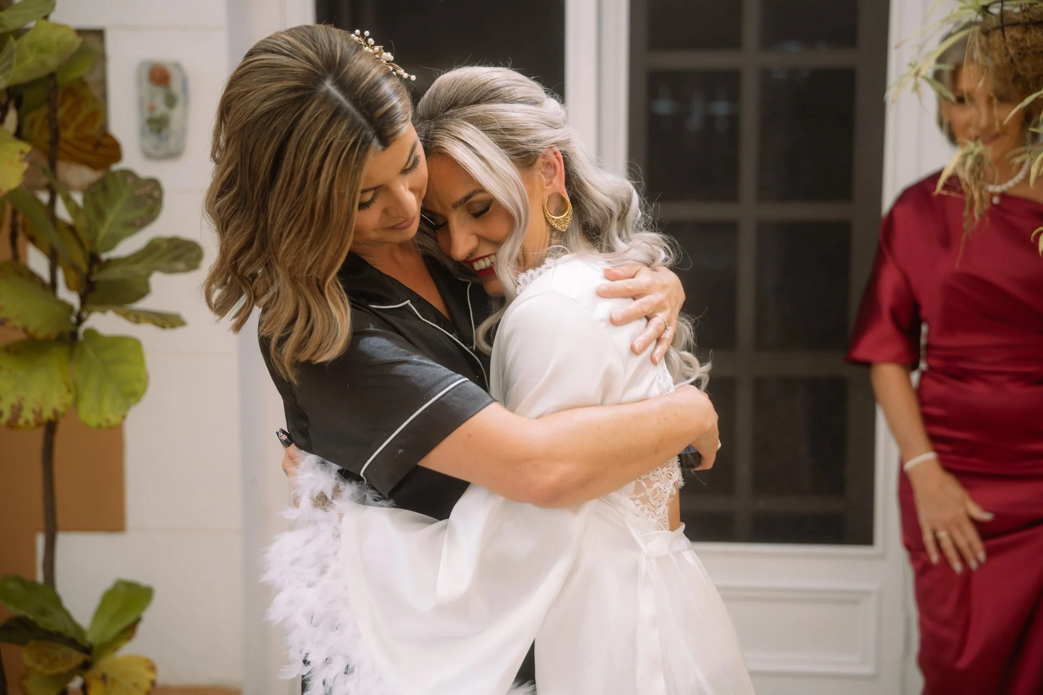 An emotional candid moment of a bride in a white feather-trimmed silk robe sharing a warm hug during morning wedding preparations at a Buckland Estate country wedding.