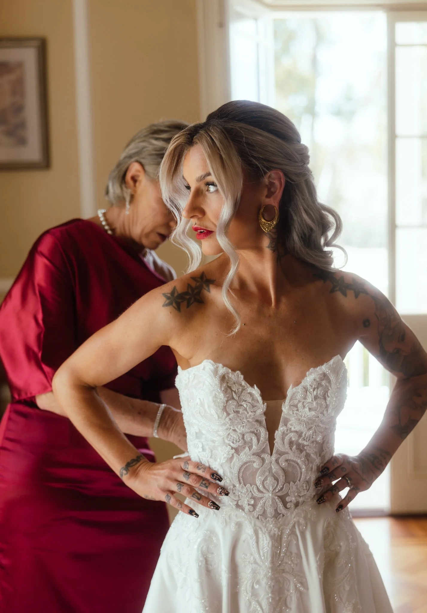 Close-up portrait of a modern bride looking over her shoulder, showcasing an intricate strapless lace bodice, elegant updo, and striking gold statement earrings inside the historic manor house.