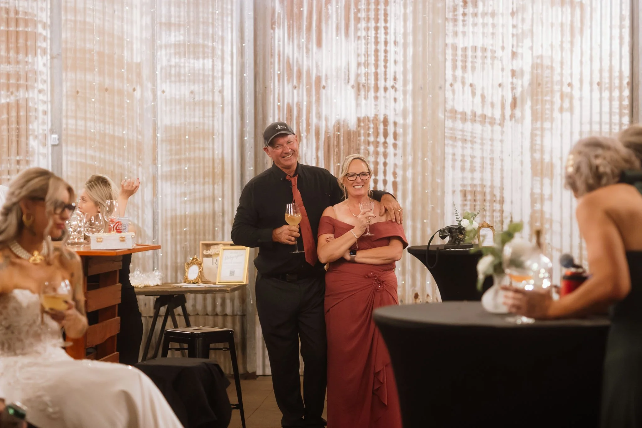 Smiling wedding guests posing for a photo inside the corrugated iron barn reception space at Buckland Estate, beautifully decorated with delicate fairy lights
