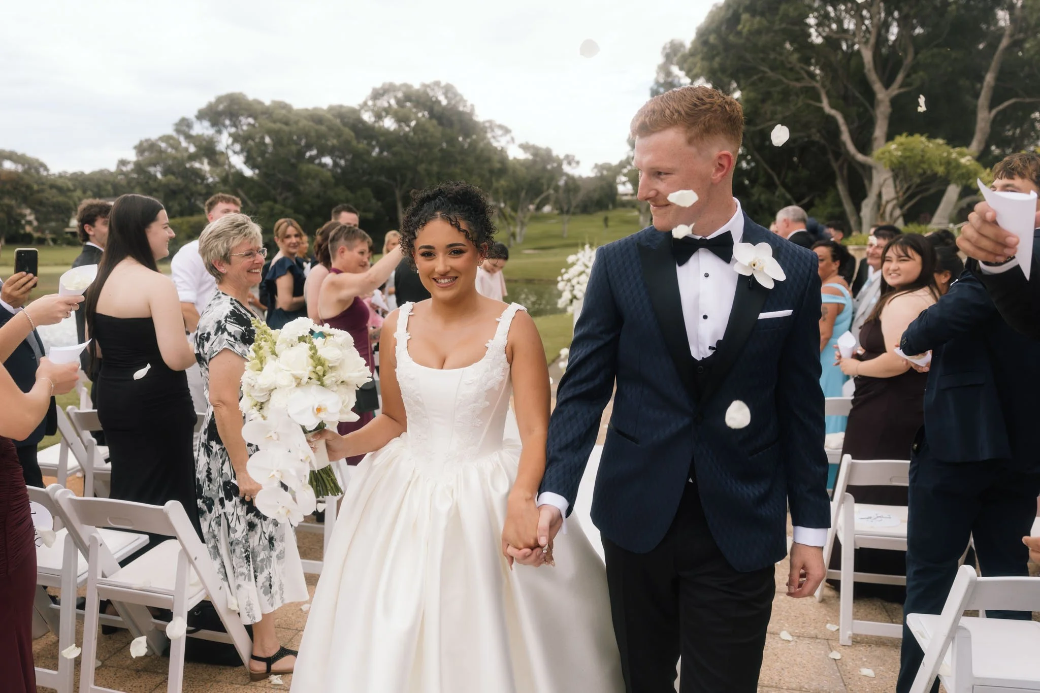 Bride and groom joyfully walking back down the aisle at Joondalup Resort Perth as guests throw white flower petals to celebrate the newly married couple, photographed by James Di Stefano
